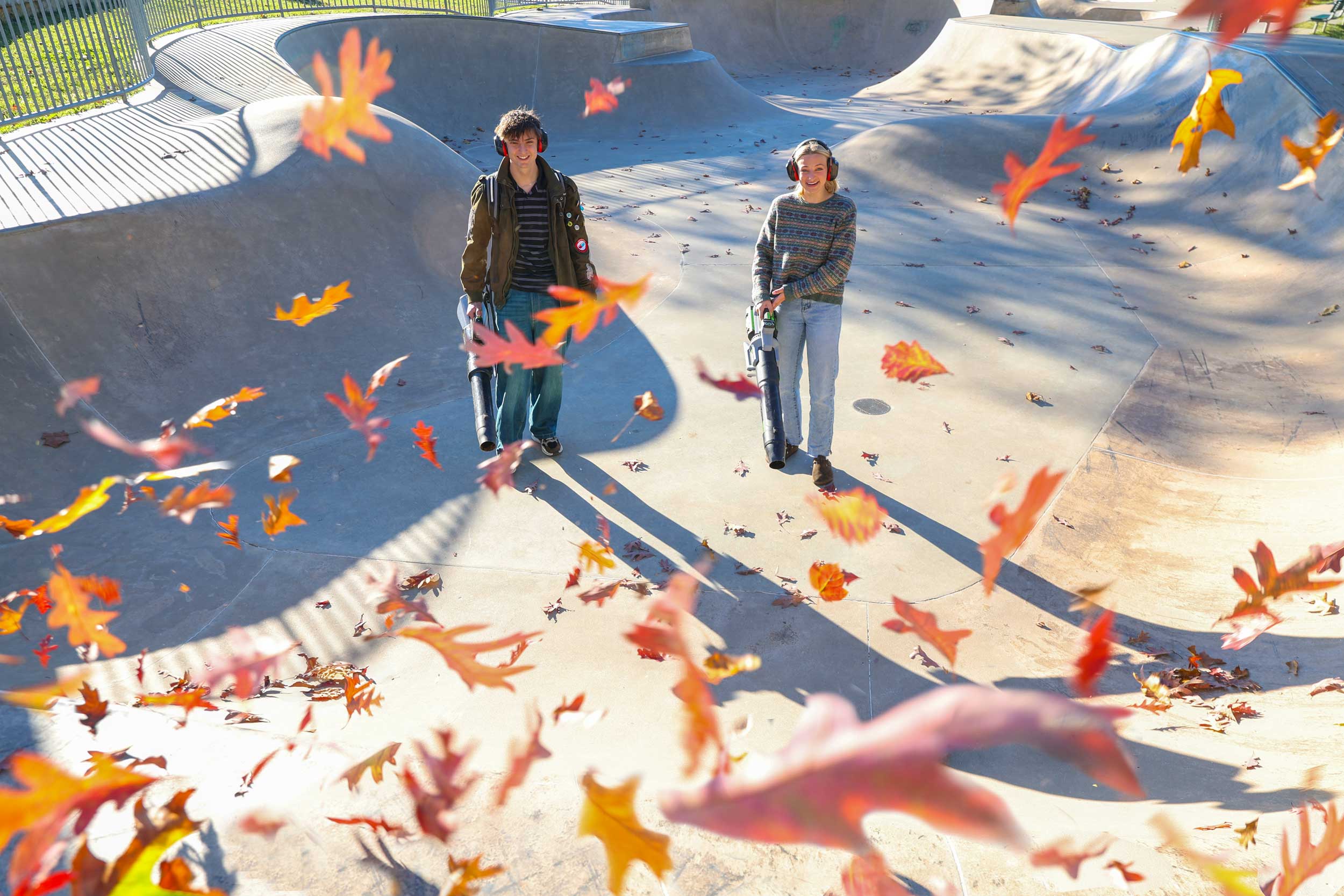 Jack Ellis and Jillian Fletcher stand in a skate park bowl that they are using leaf blowers to clear.