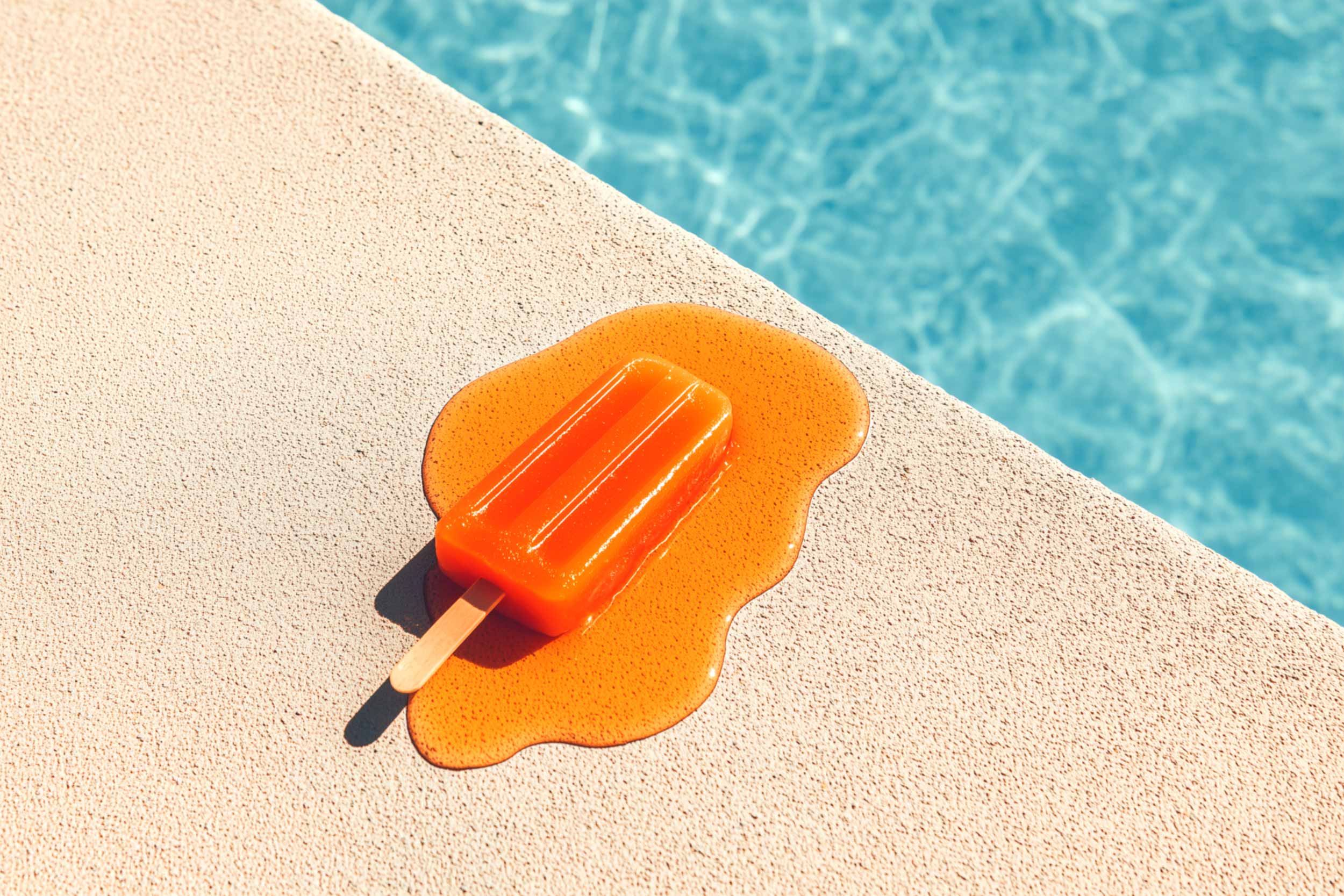 an orange popsicle melting by a swimming pool