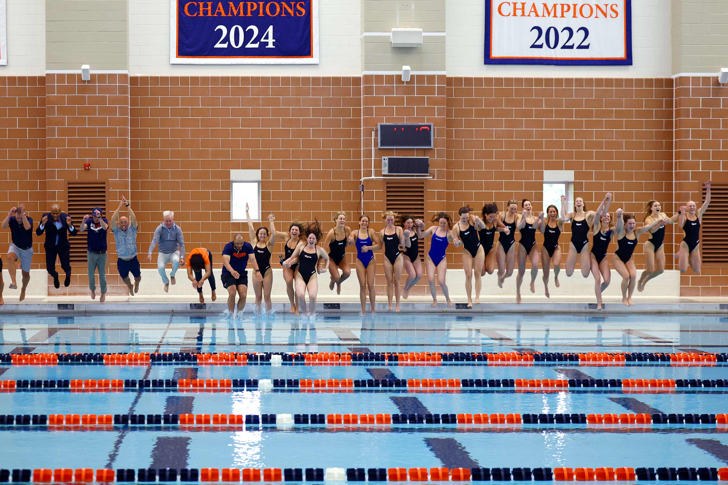 Portrait of Members of the UVA community join the Cavalier women’s swimming and diving team in a celebratory leap into the pool at the Aquatic & Fitness Center.
