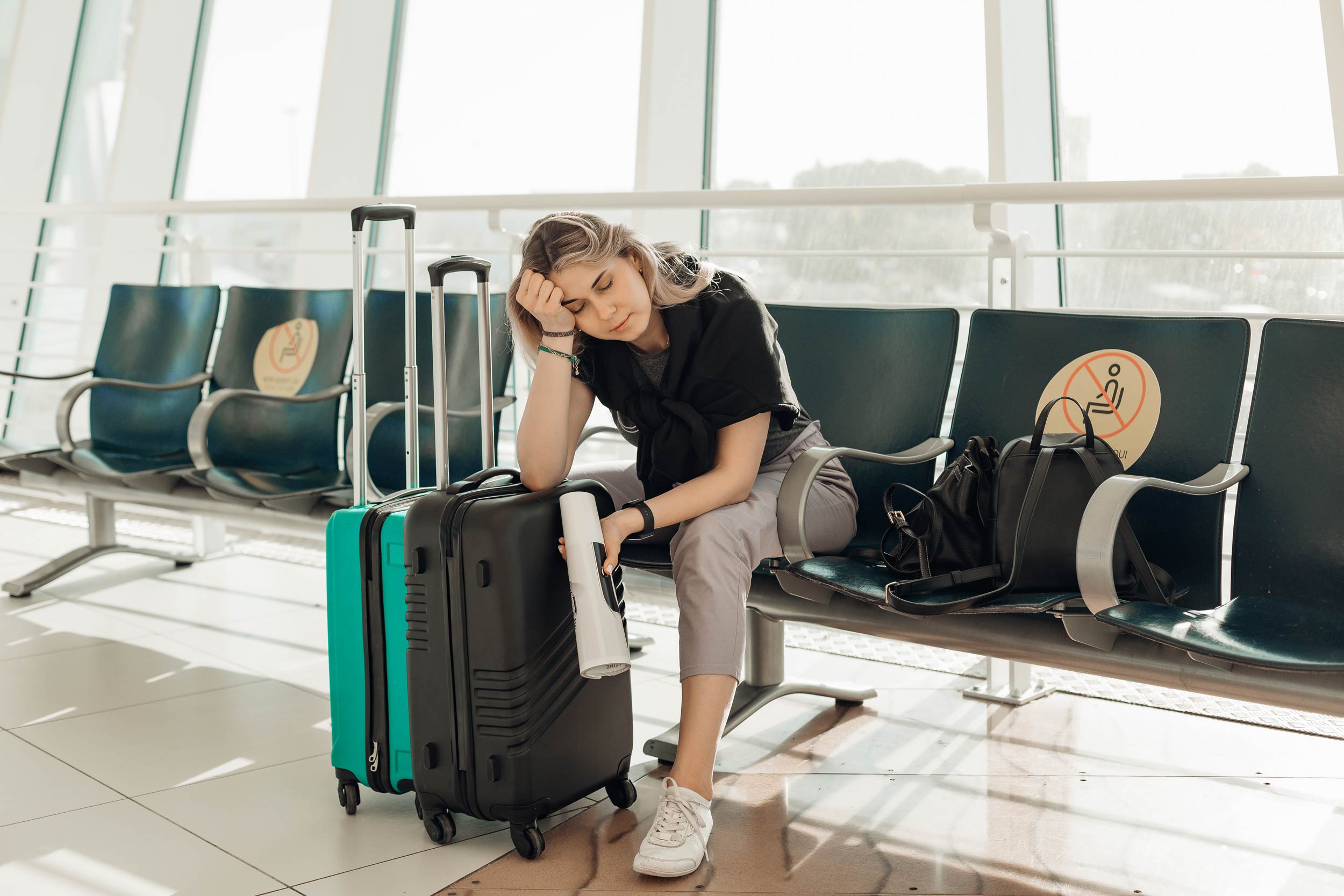 tired person sitting at an airport gate with suitcases