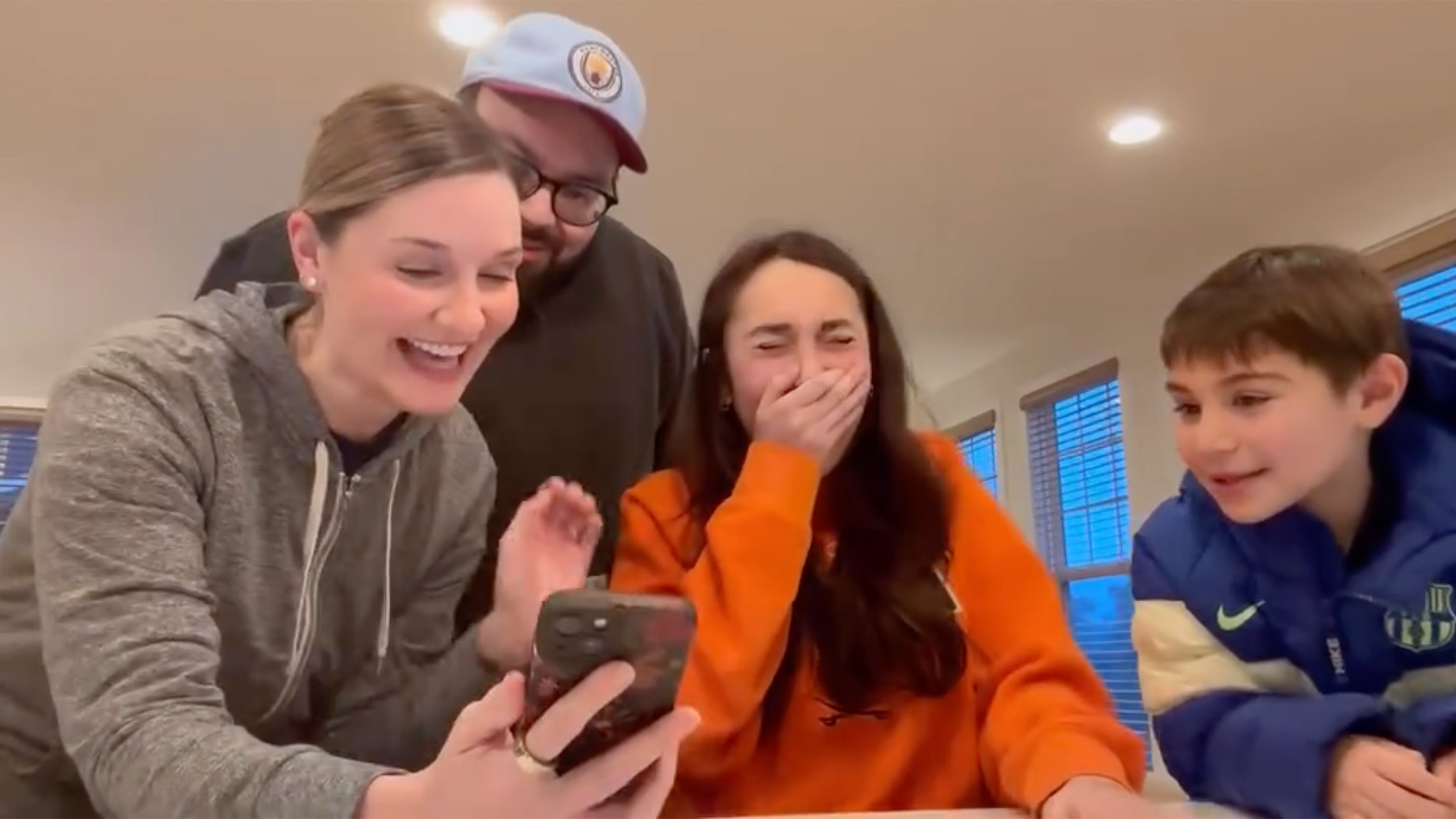 Portrait of a family showing their daughter a mobile phone with the results of her admission to the University of Virginia.