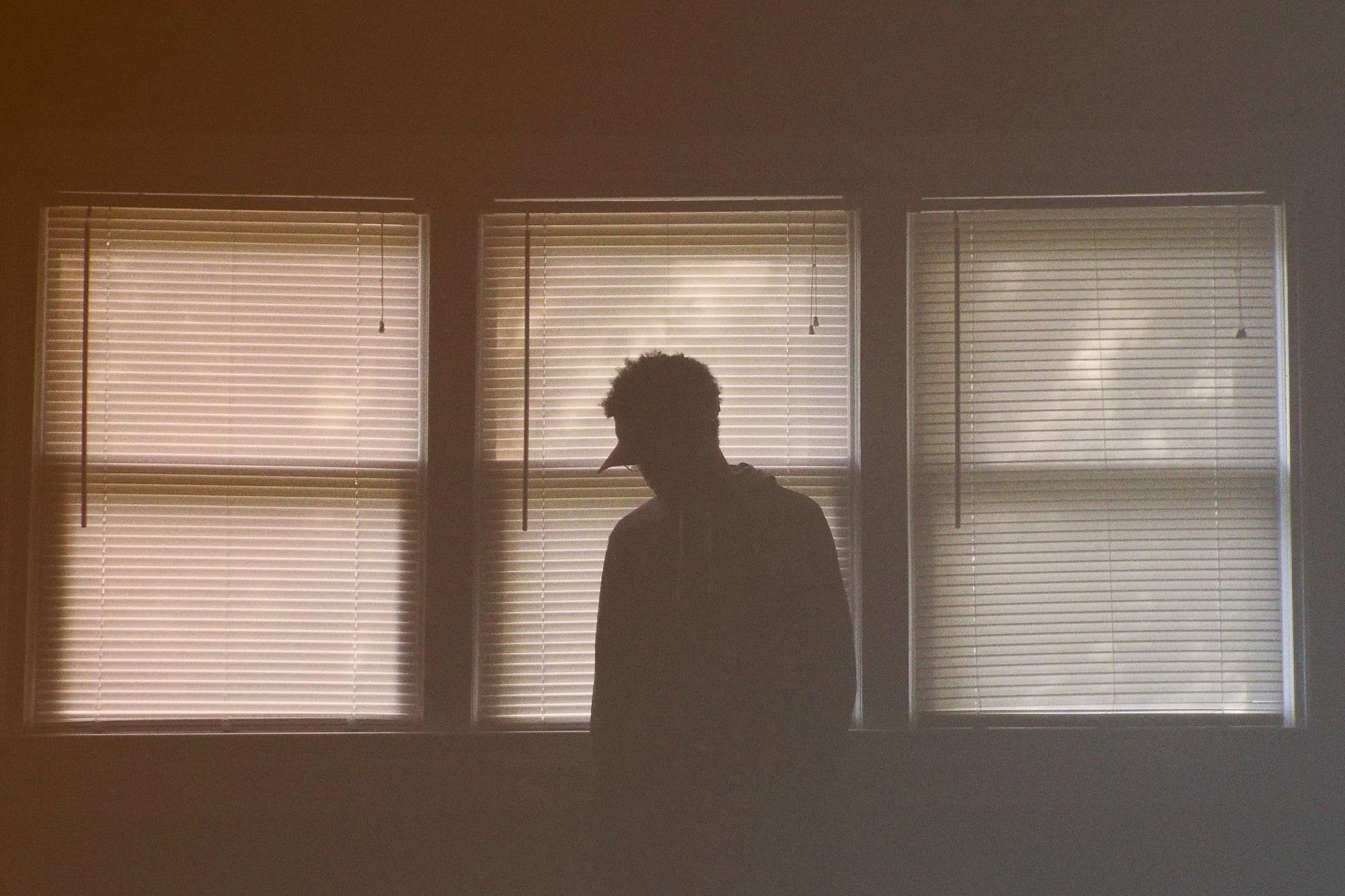 Man looking out a window with blinds drawn