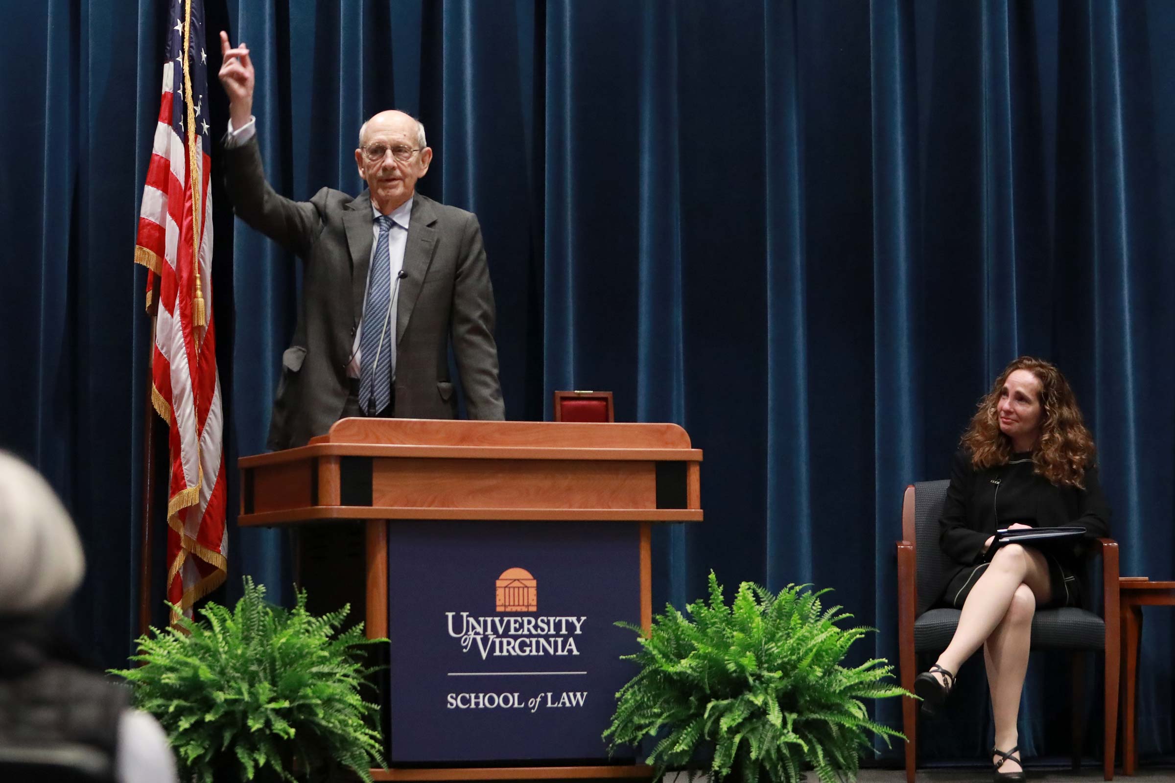 U.S. Supreme Court Justice Stephen Breyer, speaking at a podium, points a finger up. UVA Law School Dean Risa Goluboff looks on from the stage.