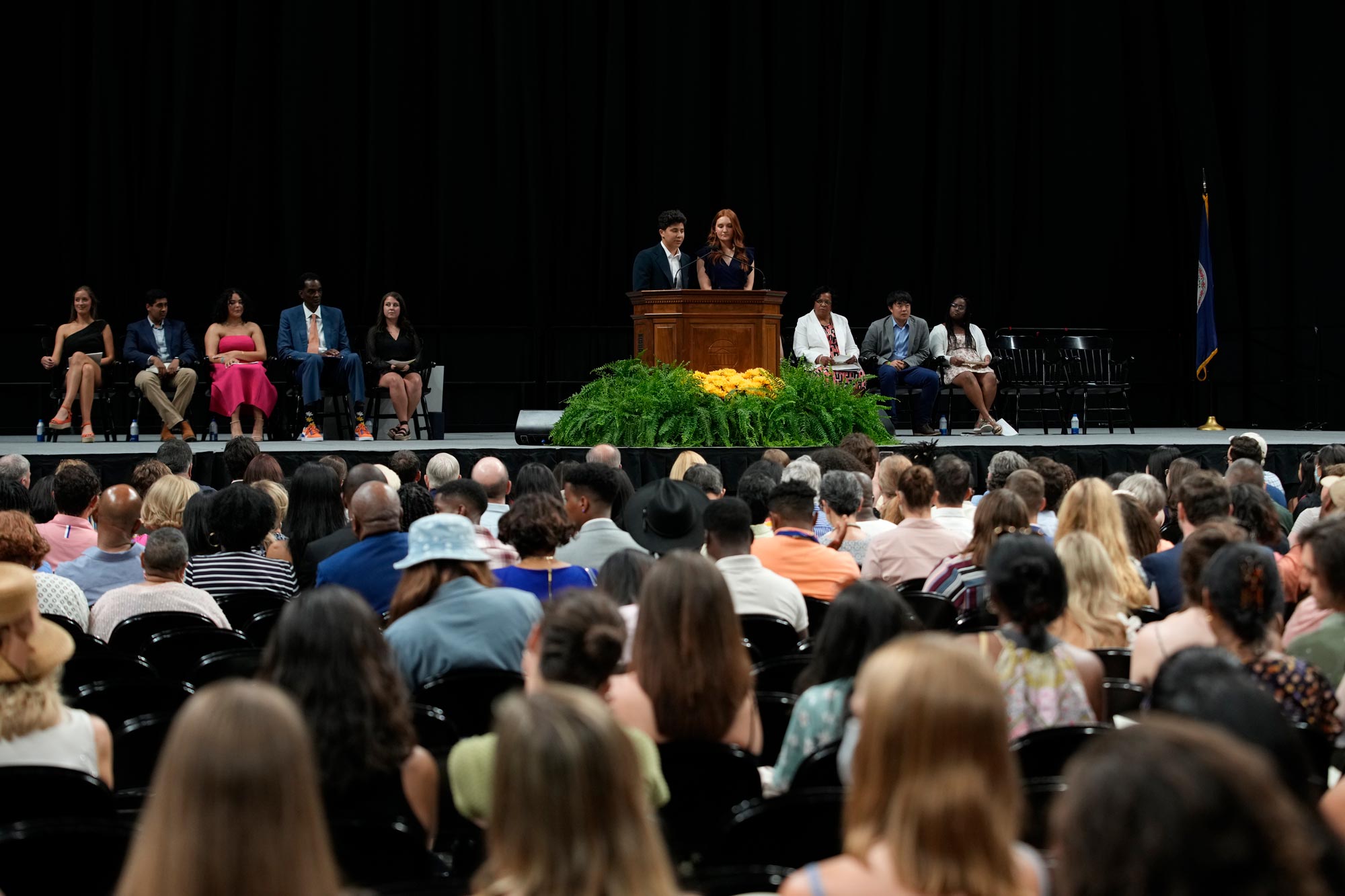 A seated crowd listens to two people speaking at a podium