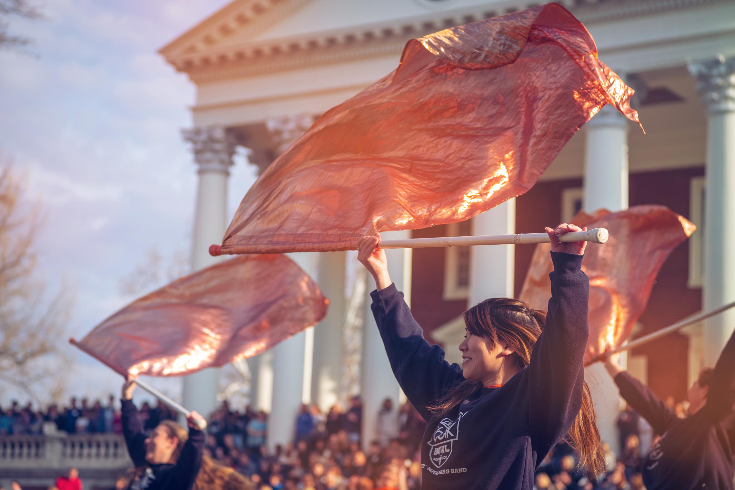 Students in black sweatshirts wave orange flags and dance in front of the UVA Rotunda