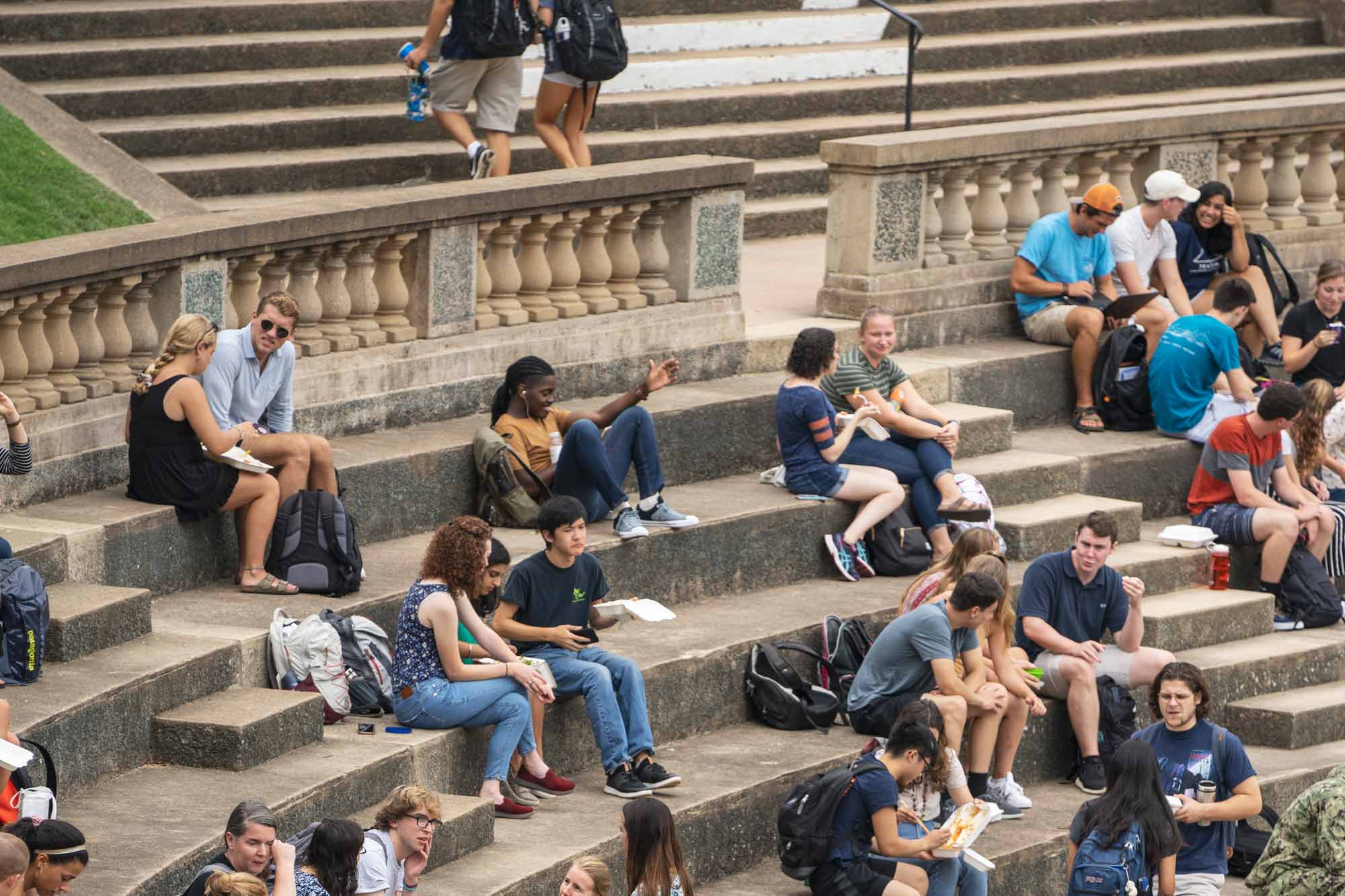 Students sit on the steps of the amphitheater talking, studying, and eating. 