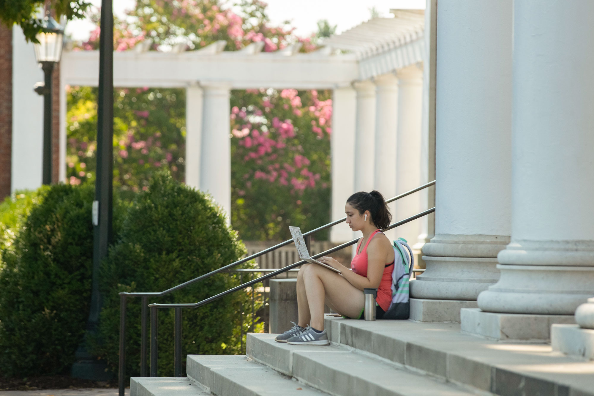 A UVA student wearing a backpack works on a laptop while seated on the steps of the Rotunda