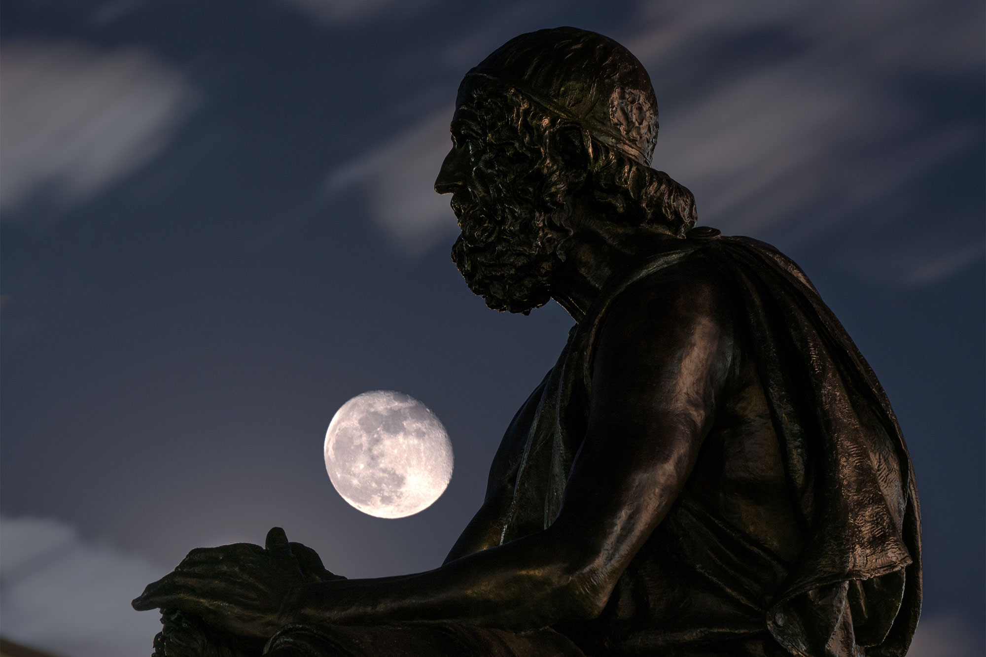 A gibbous moon is visible from the left side of UVA's Statue of Homer at night
