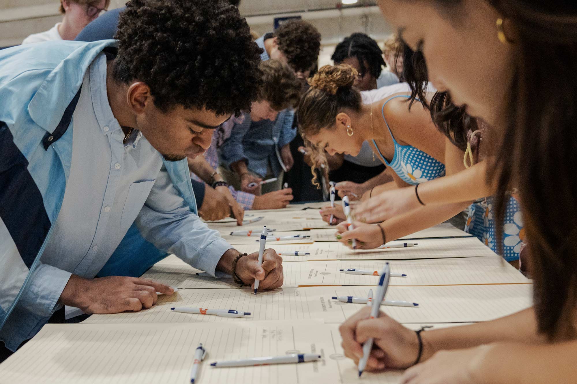 Several students lean over a long table to sign copies of the Honor Pledge