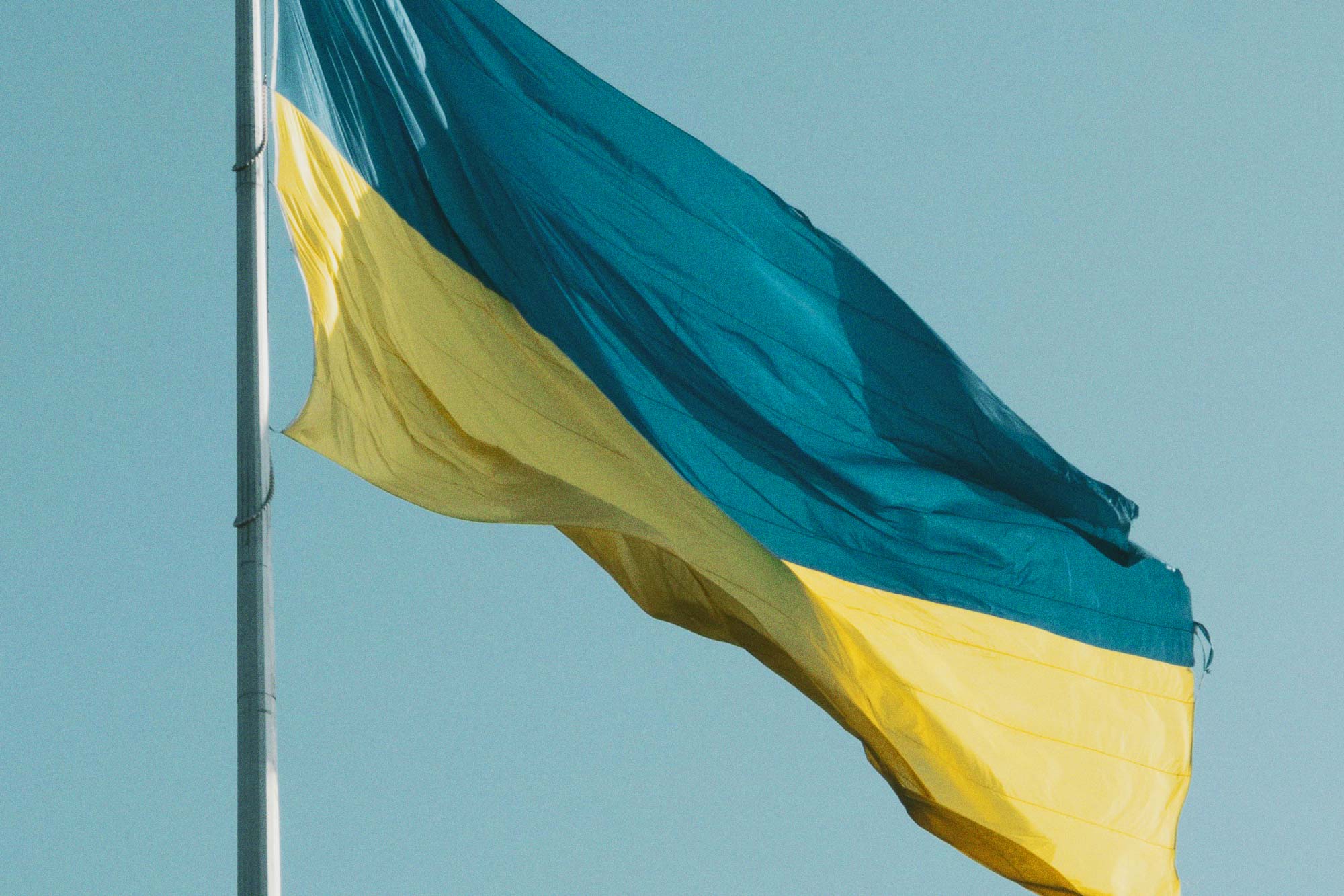 The teal and yellow flag of Ukraine flies in the wind on a clear day
