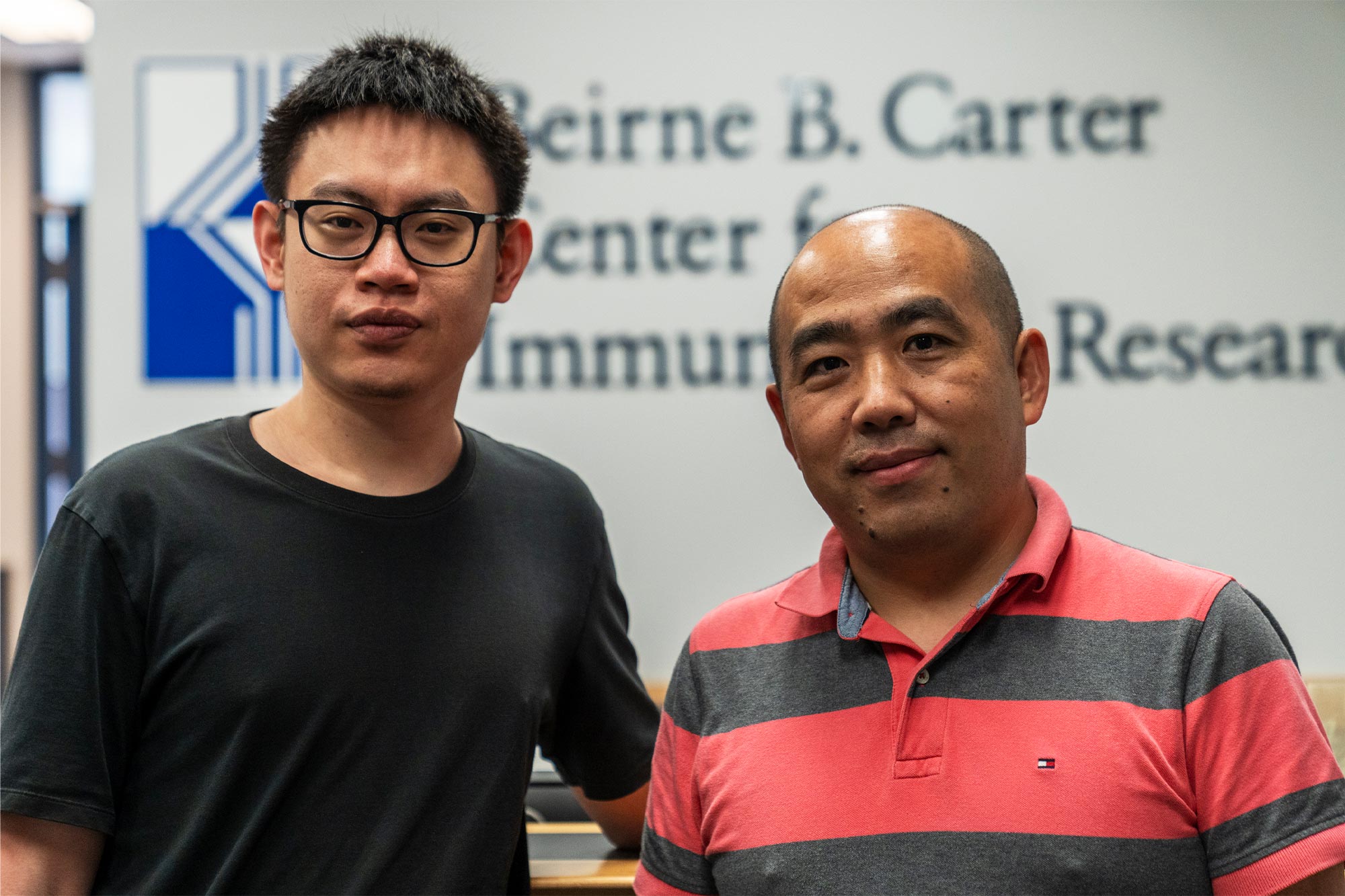 Tang and Sun stand next to each other looking at the camera in front of a sign that reads "Beirne B. Carter Center for Immunology Research"