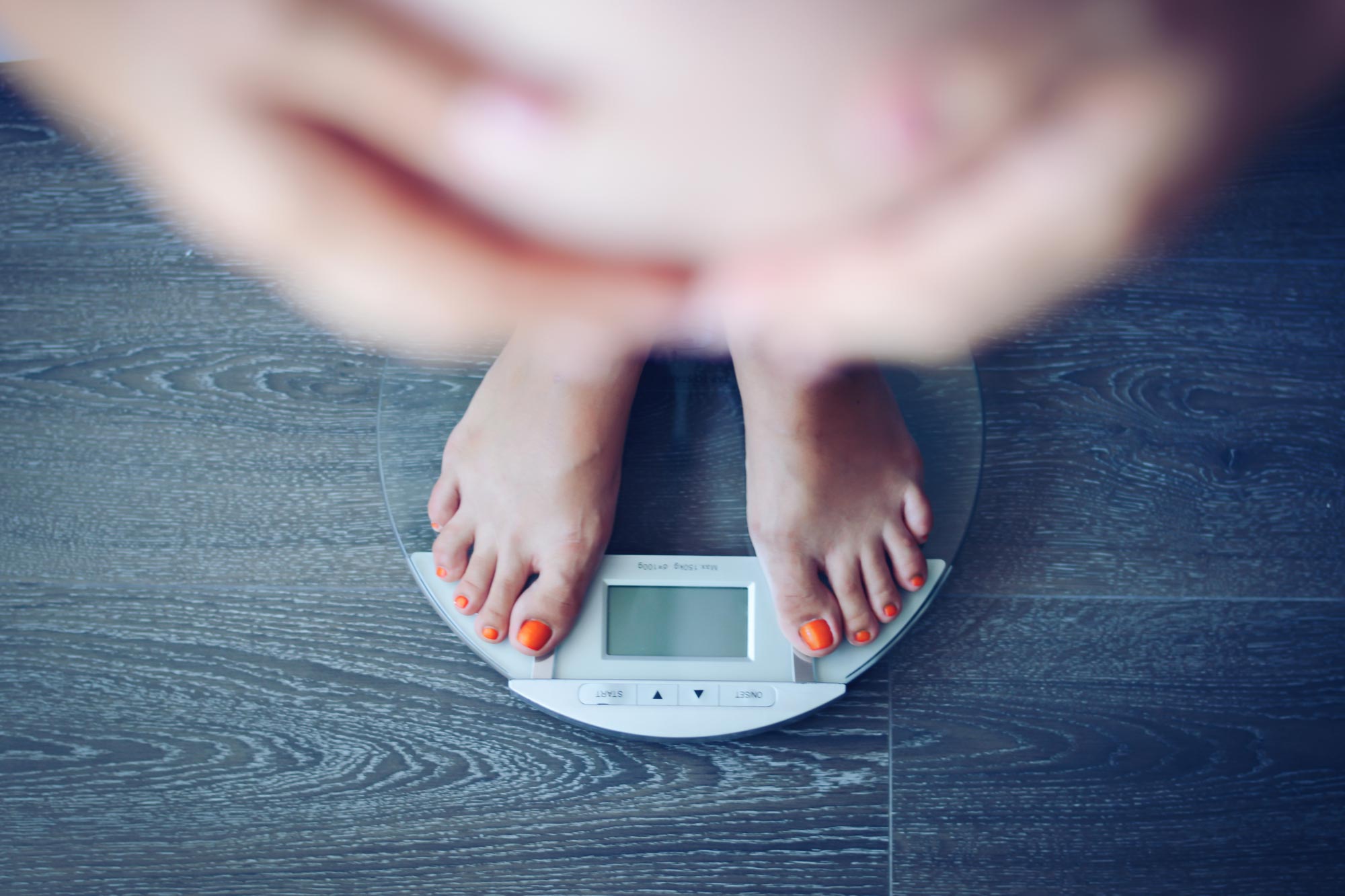 A pregnant woman weighs herself on a digital scale.