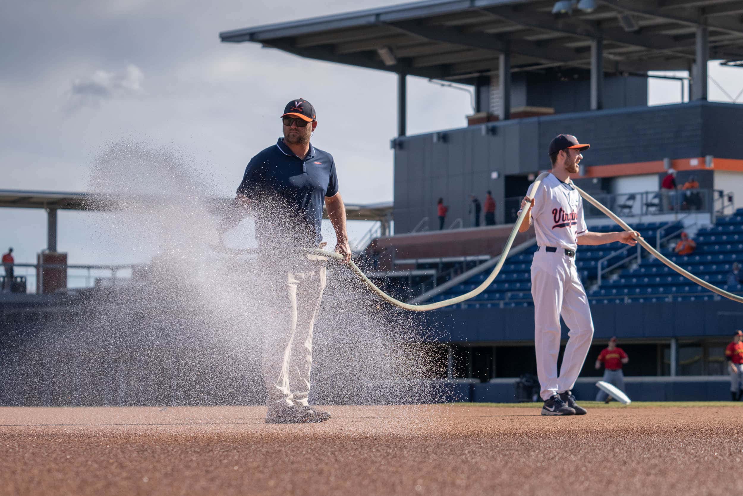 UVA staff member and baseball player watering the baseball field