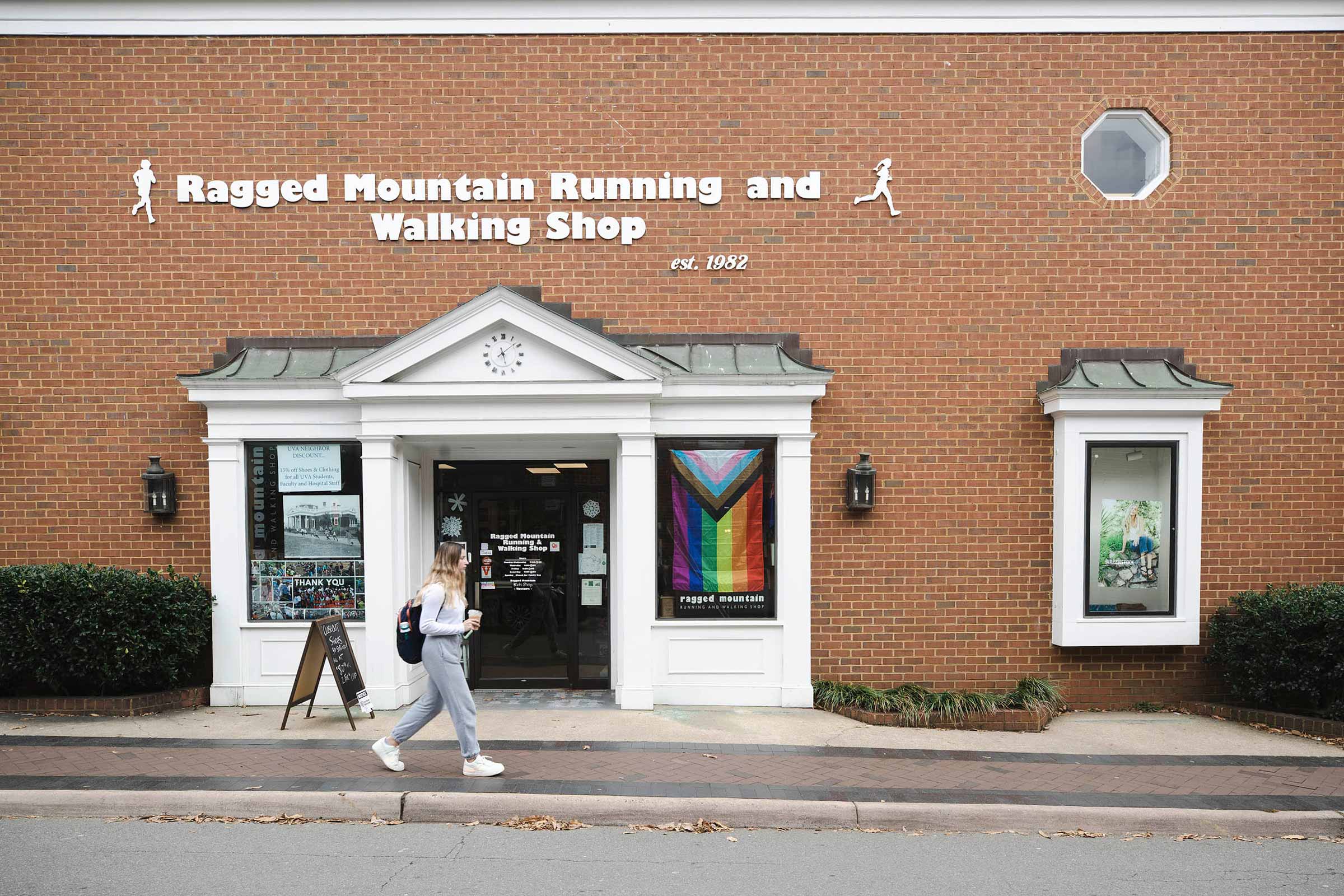 A woman walks past a storefront in a brick building with a sign reading 'Ragged Mountain Running and Walking Shop'