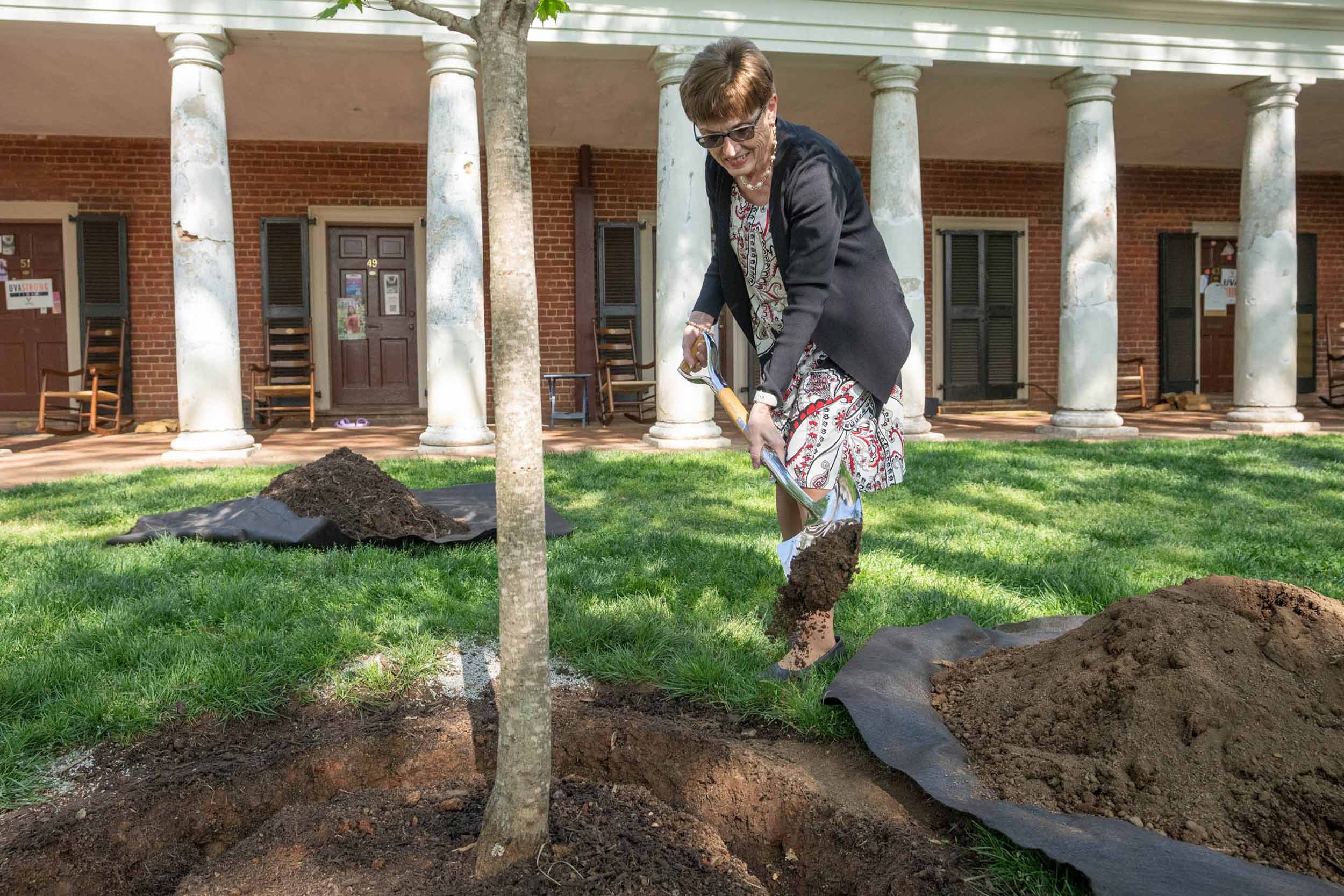 Pamela Higgins places a shovelful of dirt on the base of a tree 