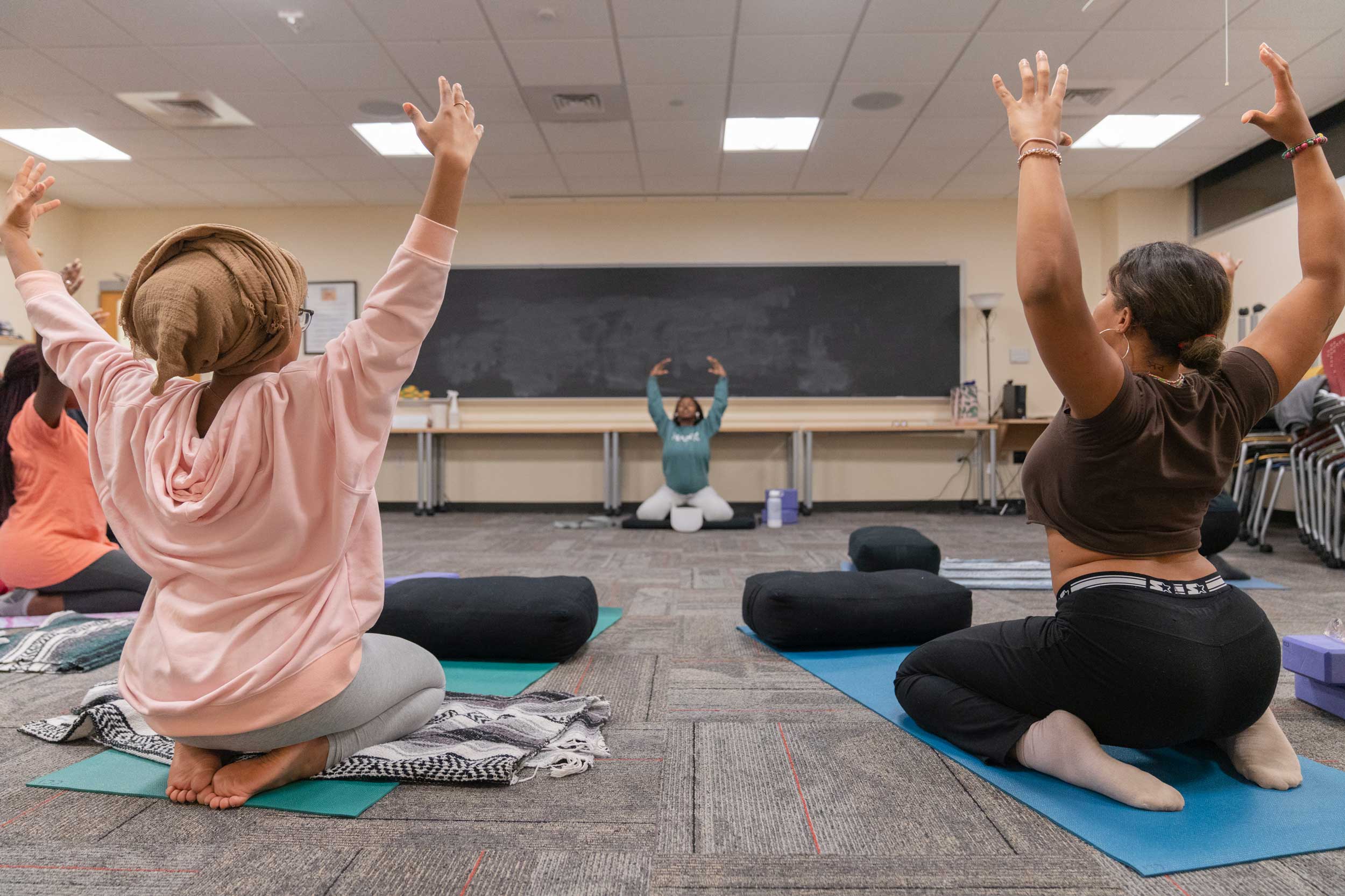 Women one their knees on yoga mats with their arms raised high in the air
