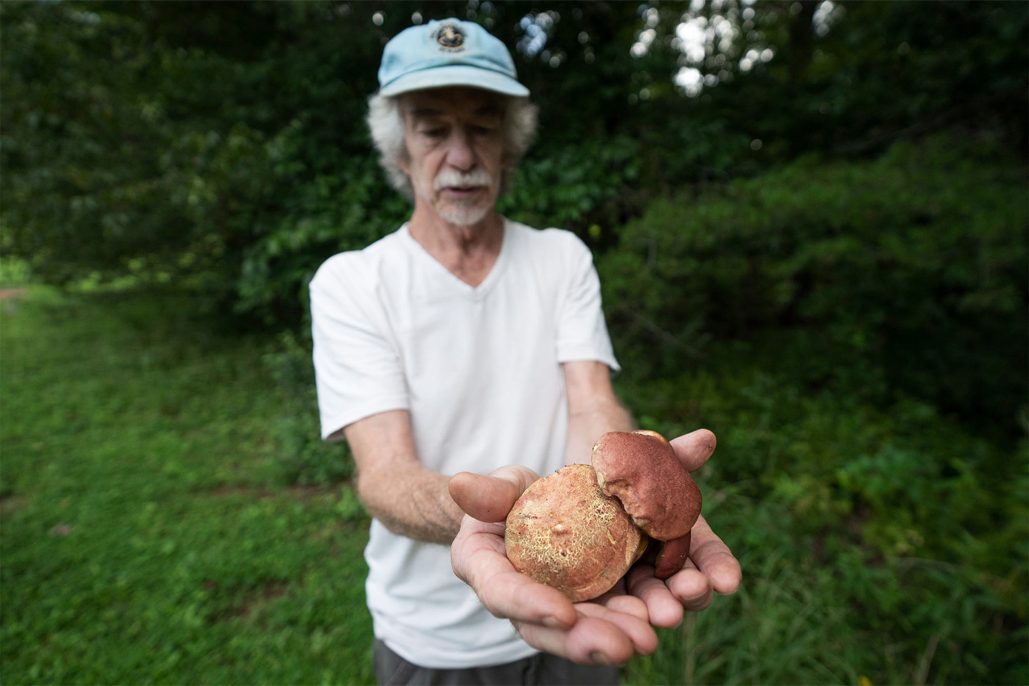 Tim Andrus stands in a clearing, holding two large mushrooms toward the camera