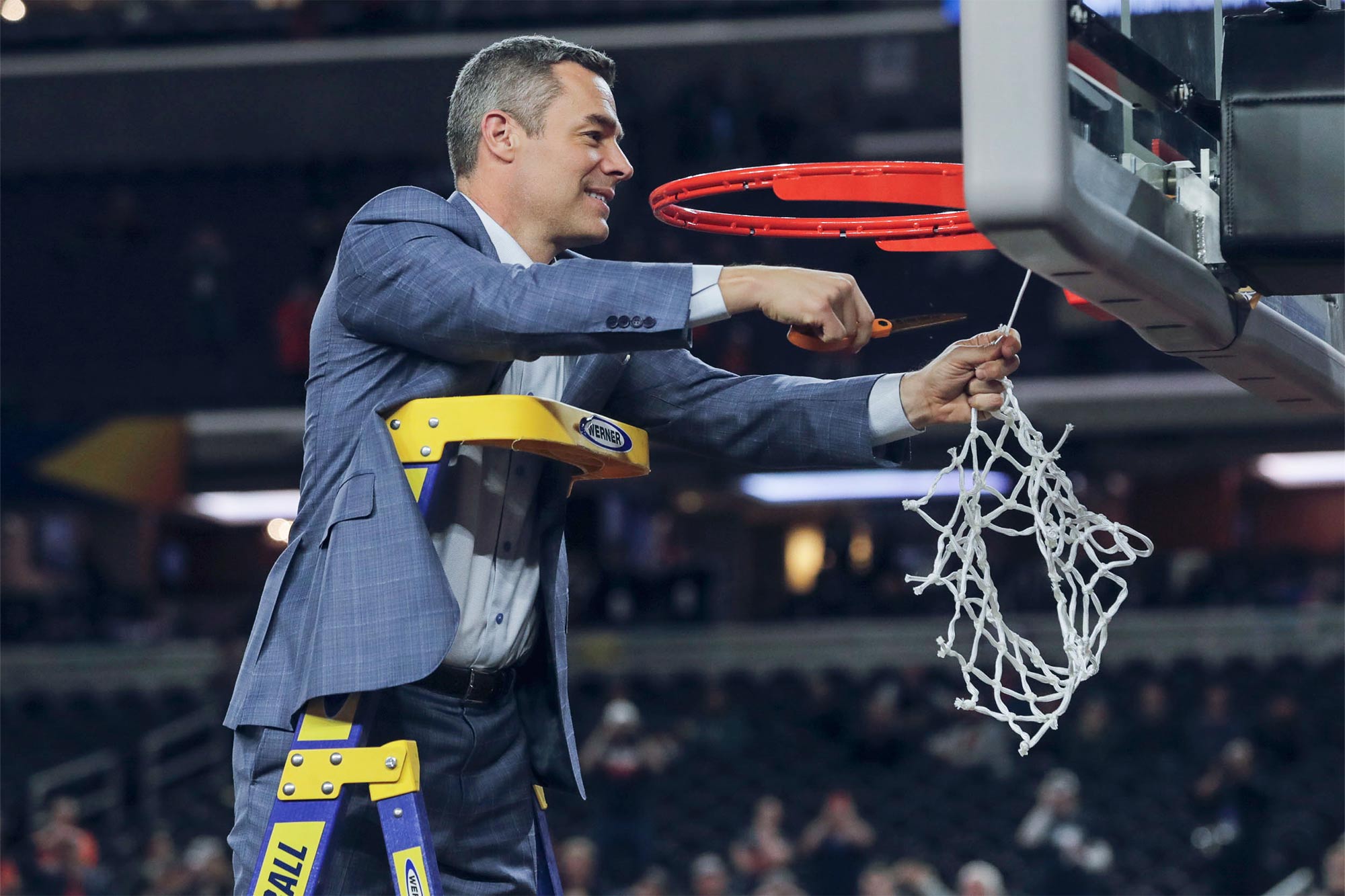 Tony Bennett stands on a ladder and cuts down the net from a basketball hoop