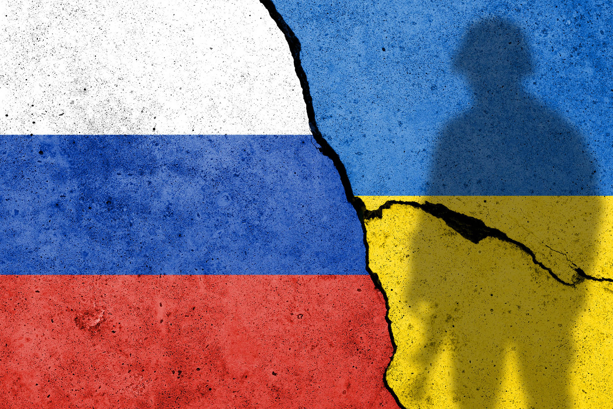 Russian flag on left and ukraine flag on right with a shadow of a soldier and crack between the flags and down the Ukraine flag.