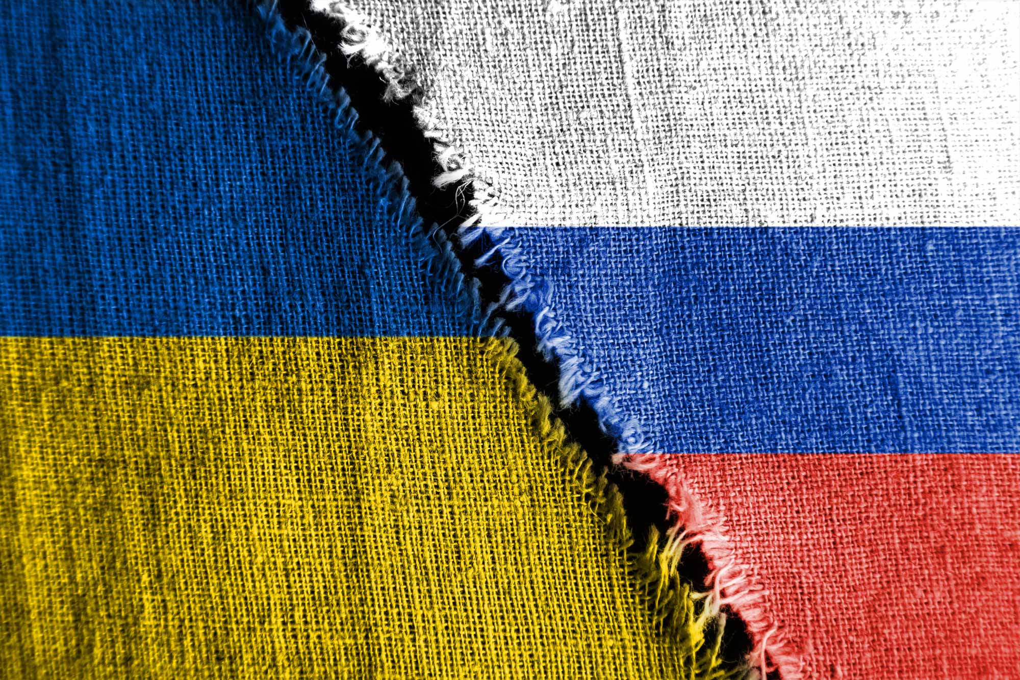 Ukraine flag on the left with frayed ends next to and a Russian flag on the right with frayed ends.  Black gap between them