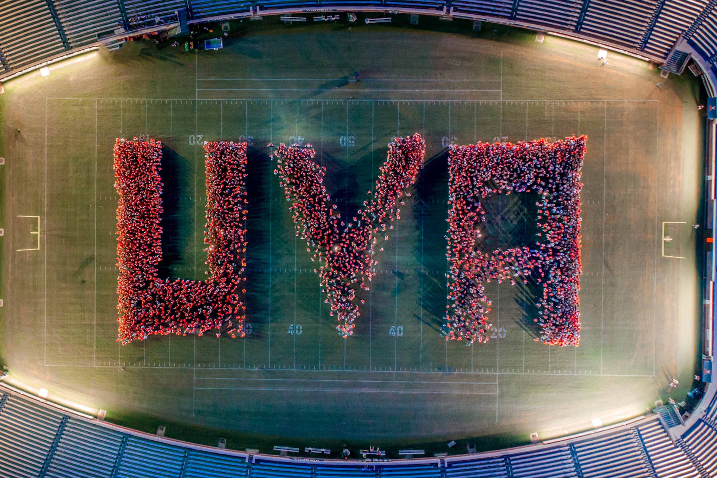 An aerial view of students wearing orange shirts and standing in formation to spell UVA