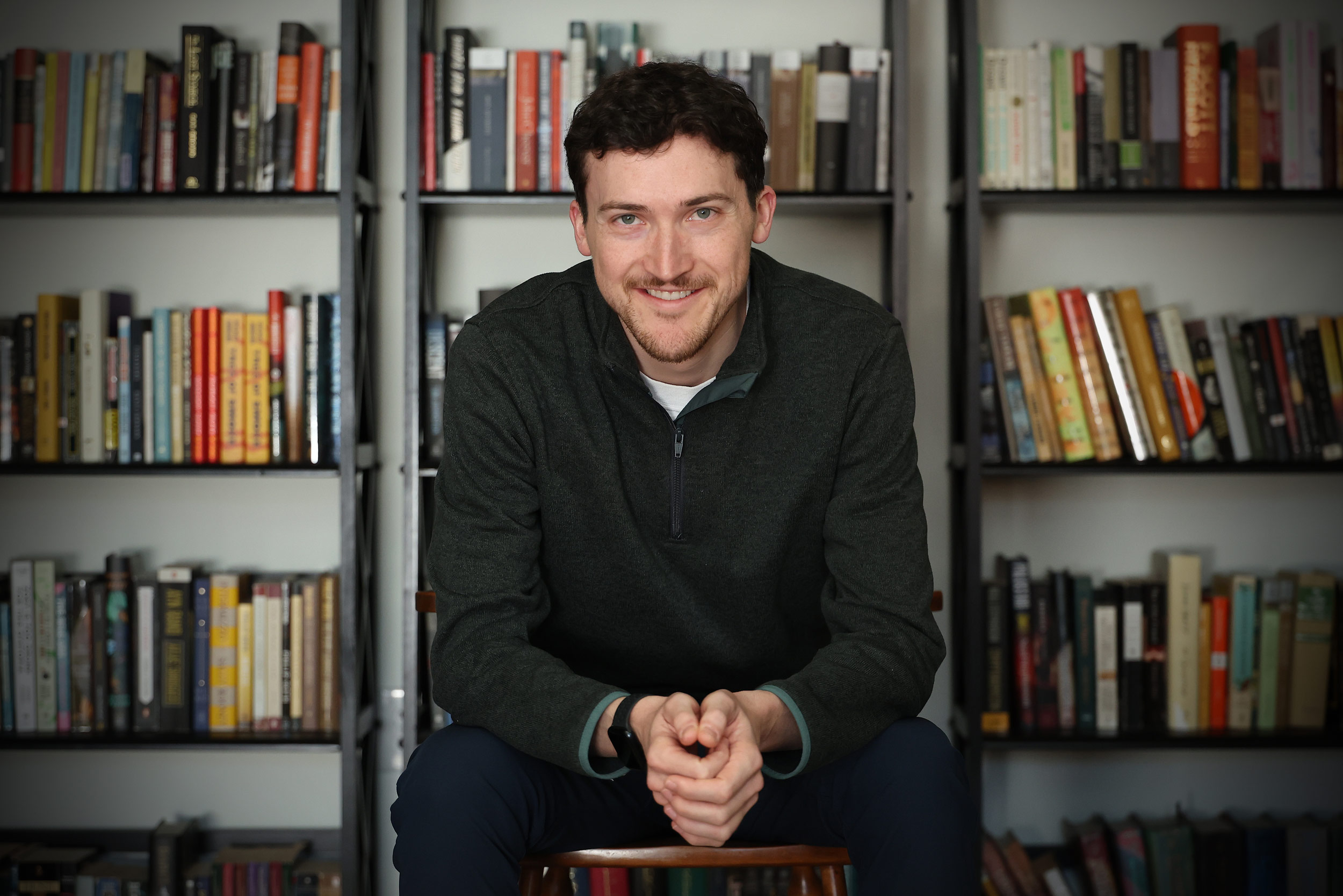 William Dozier smiling and looking at the camera in front of his collection of books