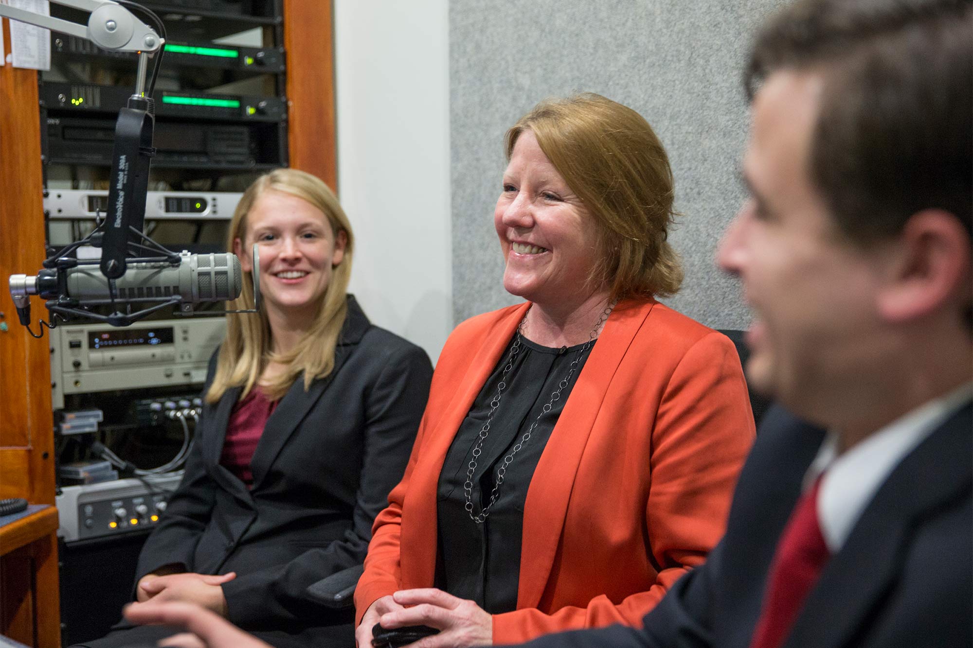 Two women and a man smile and talk into microphones