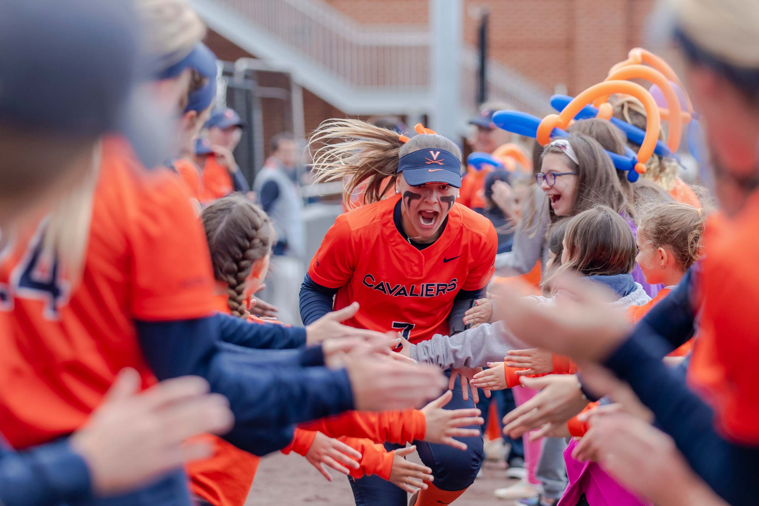 A uniformed UVA softball player runs through a high-five tunnel of young girls and teammates.