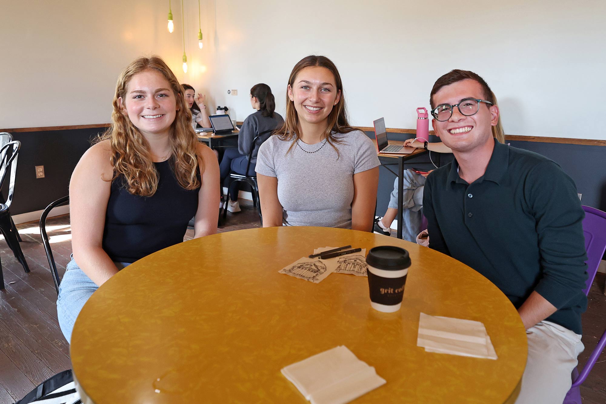 Carly Batson, Anna Travasos and Cole Rozwadowski sitting togehter at a table with napkins to sketch upon