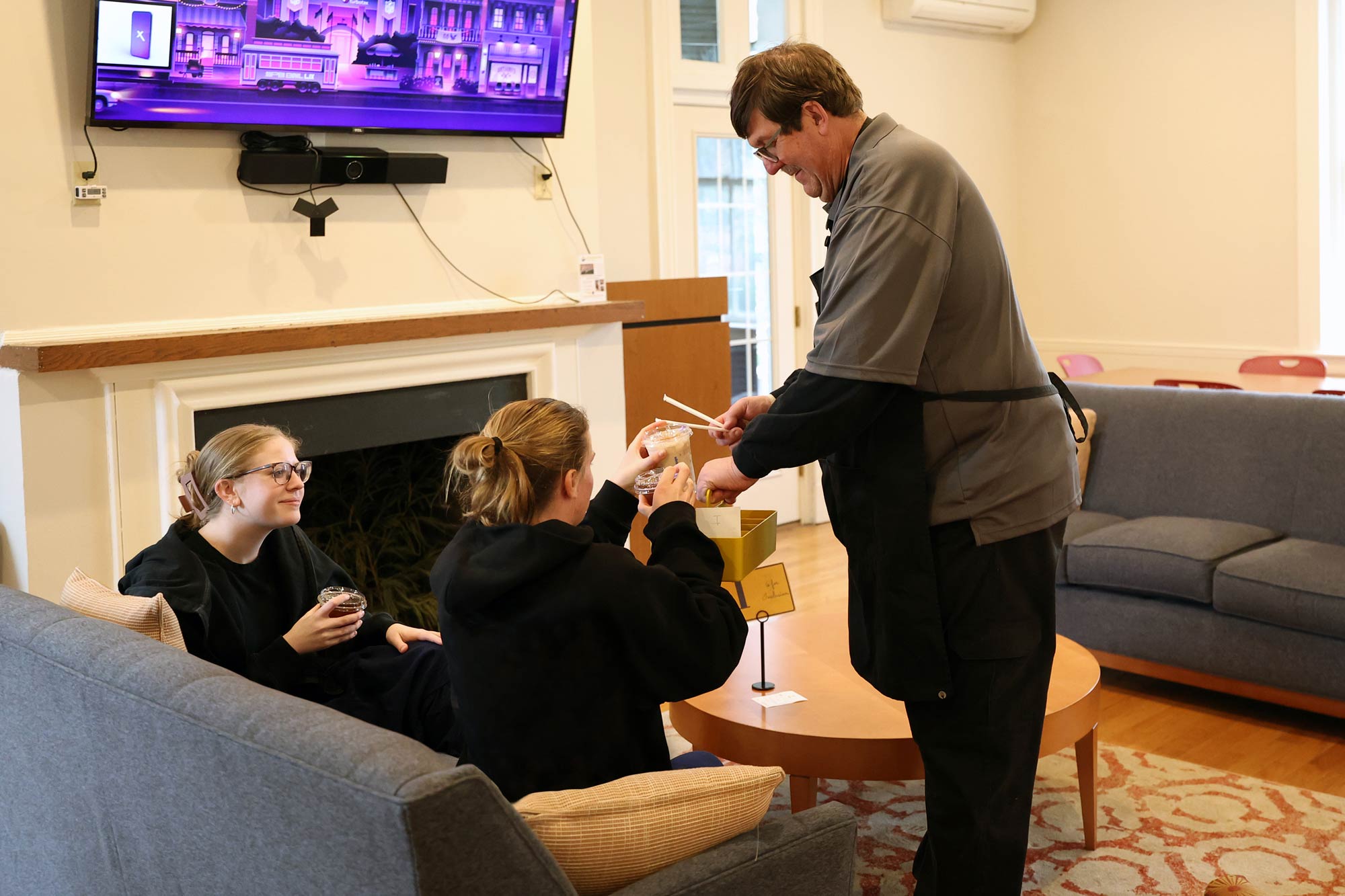 Portrait of Kindness Café employee Charlie Scott serving drinks to third-year students Penelope Molitz and Nicole Cruthirds.