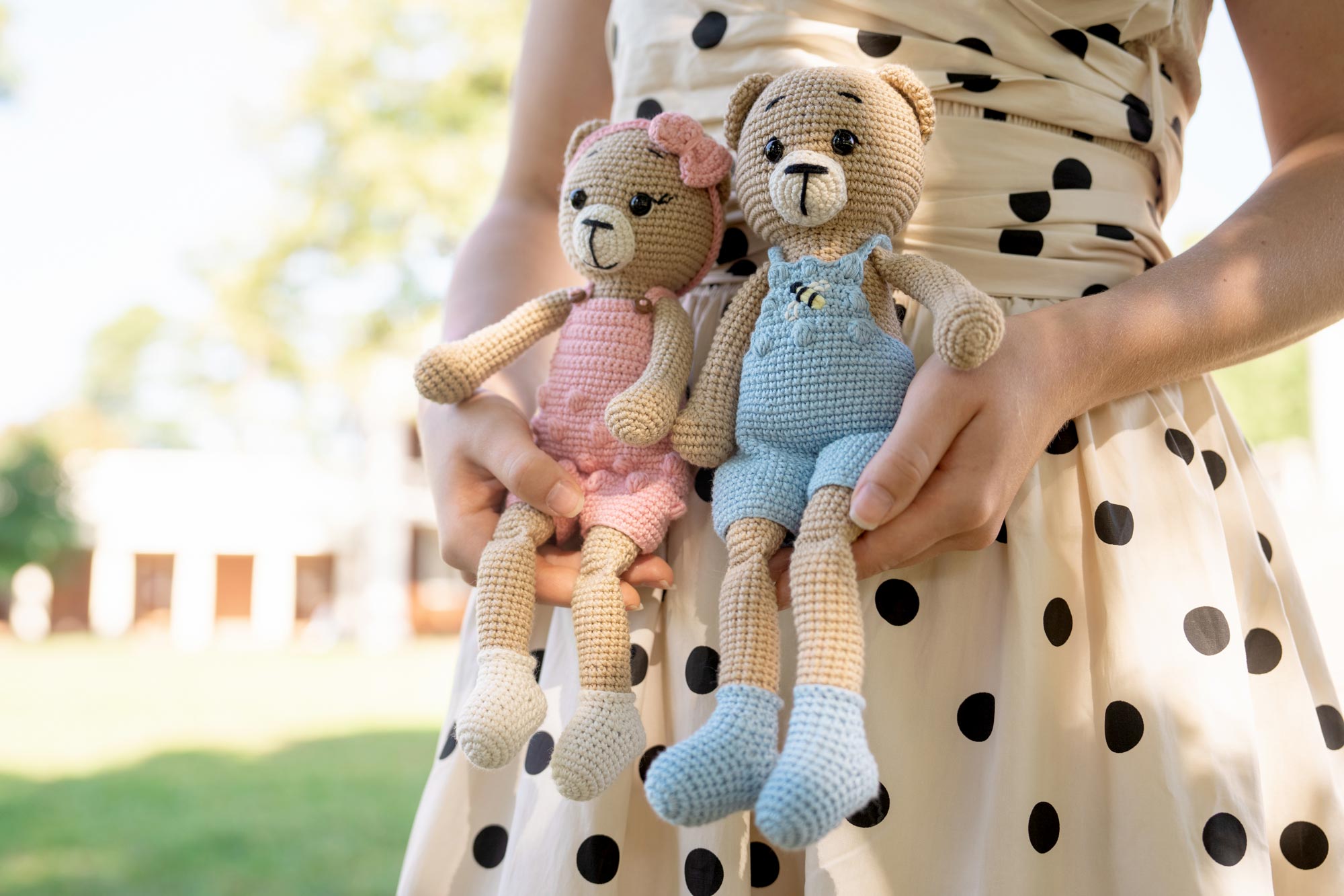 Portrait of a person holding two crocheted bear toys.