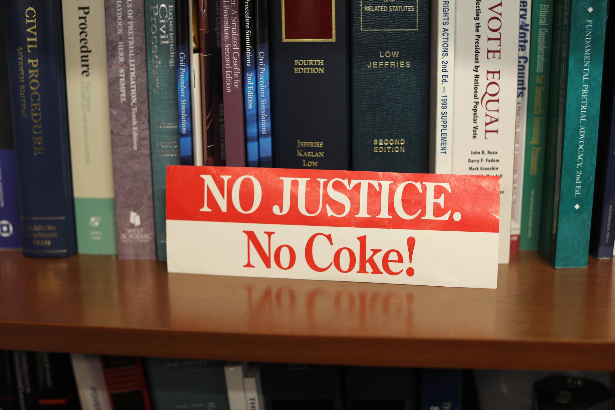 Portrait of a sticker on a bookshelf that says 'No Justice. No Coke!