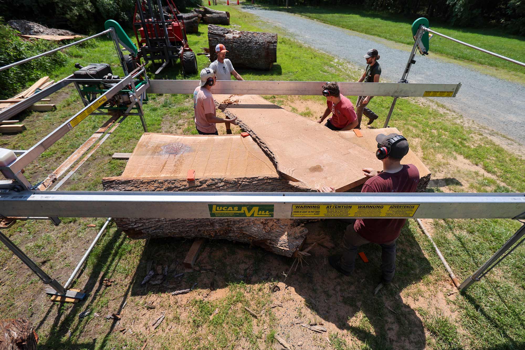 Portrait of UVA Sawmilling workers slide a slab of wood from an 11-foot-long white oak log.
