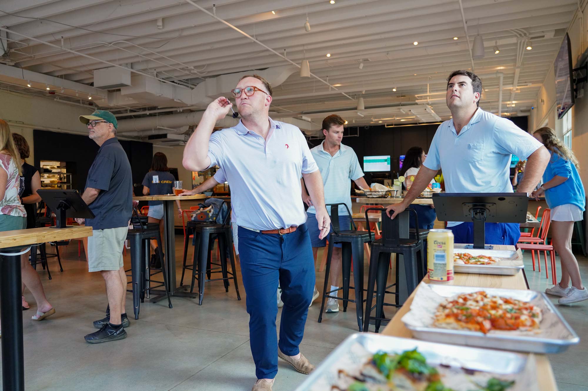 A portrait of a person throwing a dart, with others watching.