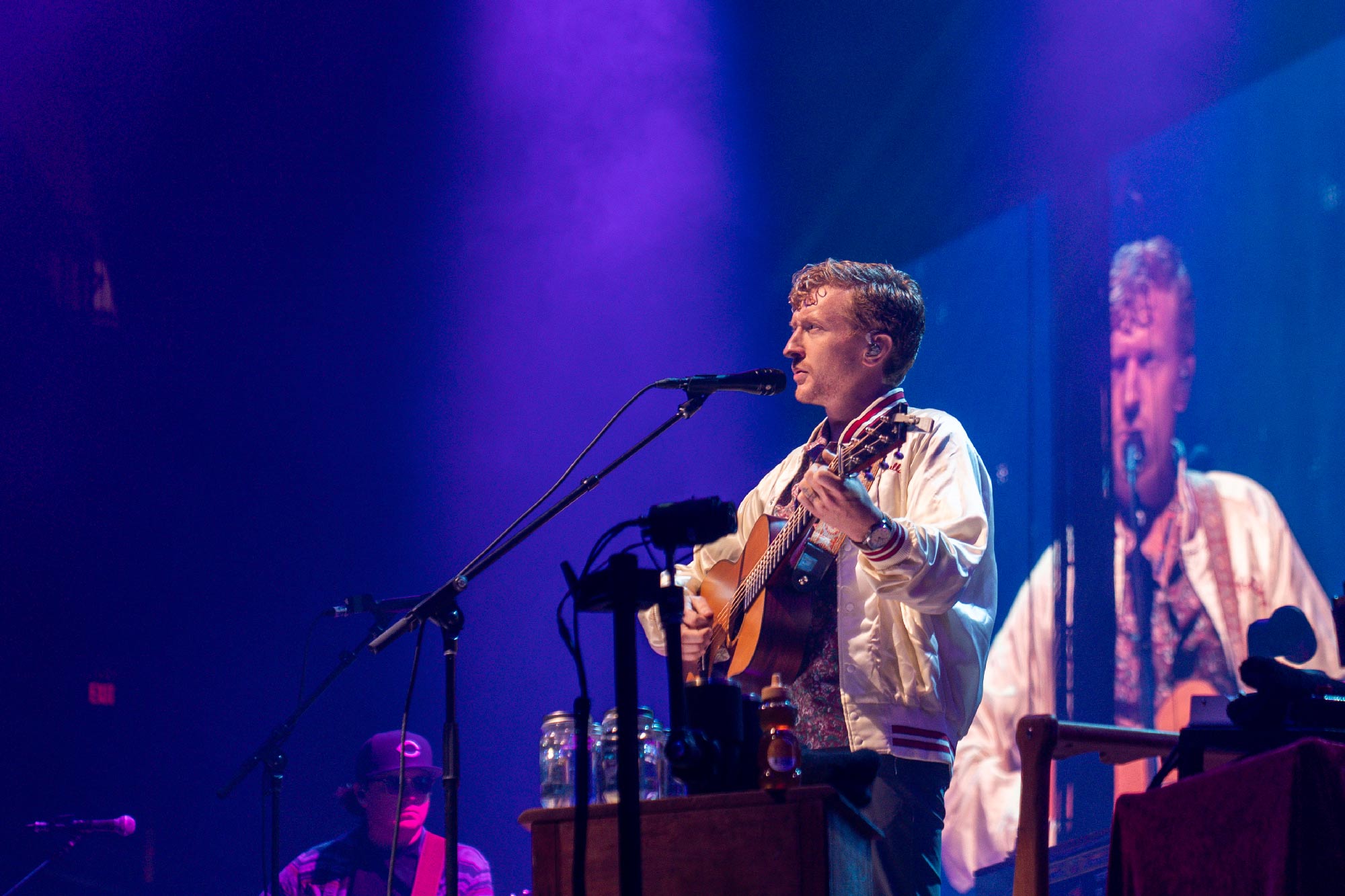 Tyler Childers holding his guitar and singing at UVA's John Paul Jones Arena in front of a jumbotron 