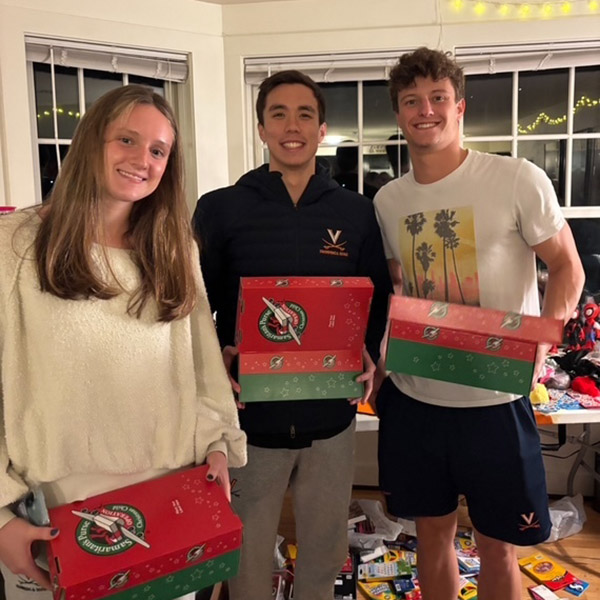 Three UVA swimmers holding red and green gift boses they had packed
