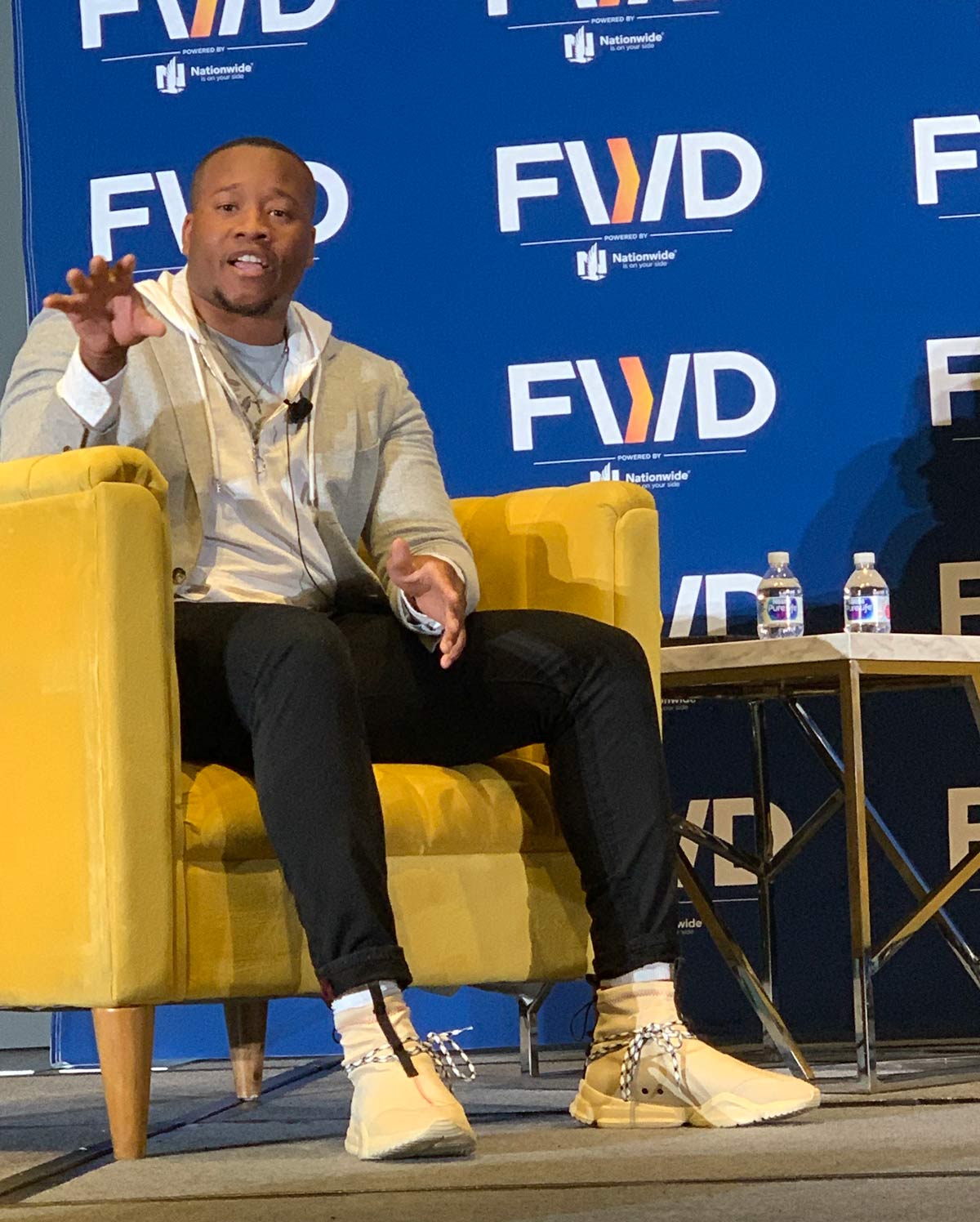 Minnifield sitting on a stage with a background that repeats the logo ‘FWD’.