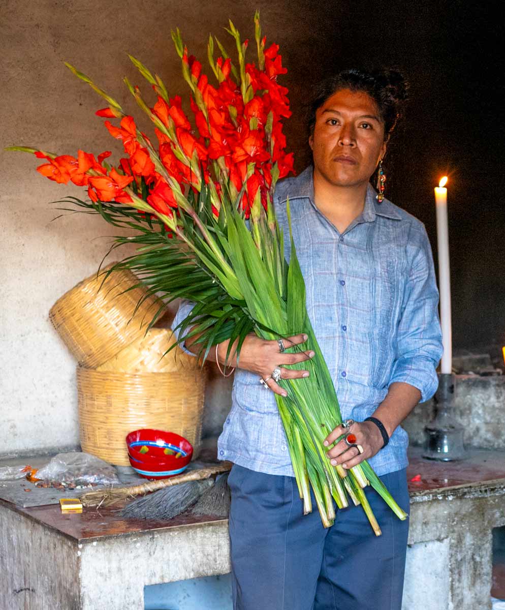 Federico Cuatlacuatl holding several cut flowers in a darkened outside structure lit by a candle.