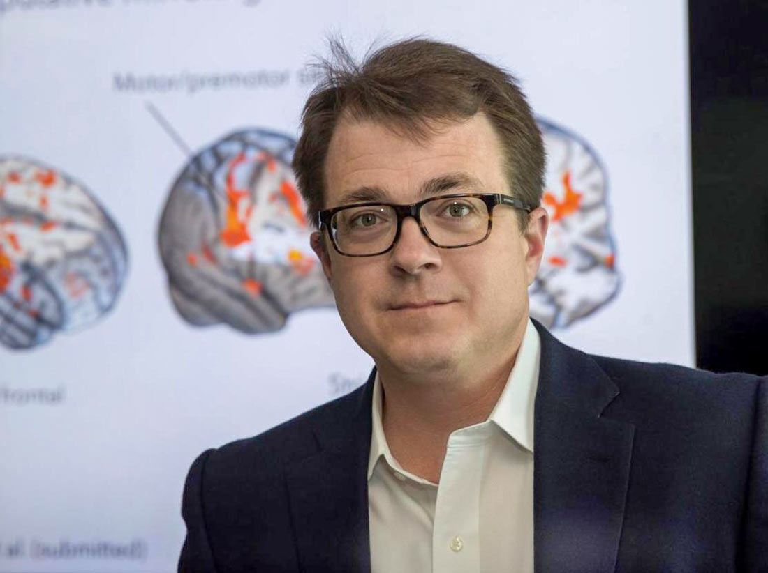 Kevin Pelphrey in front of several diagrams of brain activity zones during different stimuli