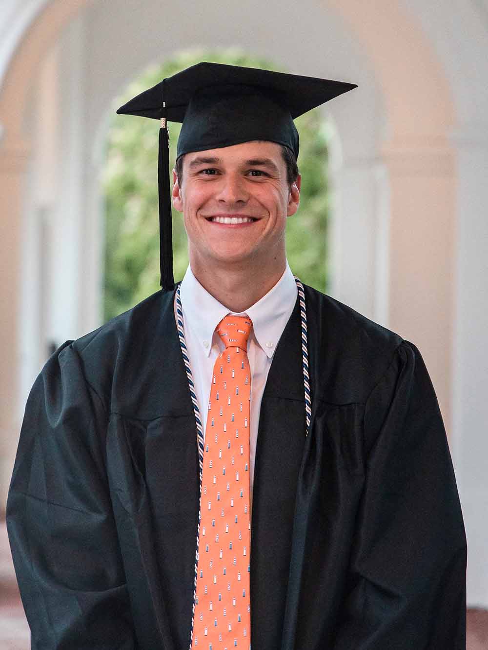Portrait of Justin Grender in his graduation cap and gown on the UVA Lawn