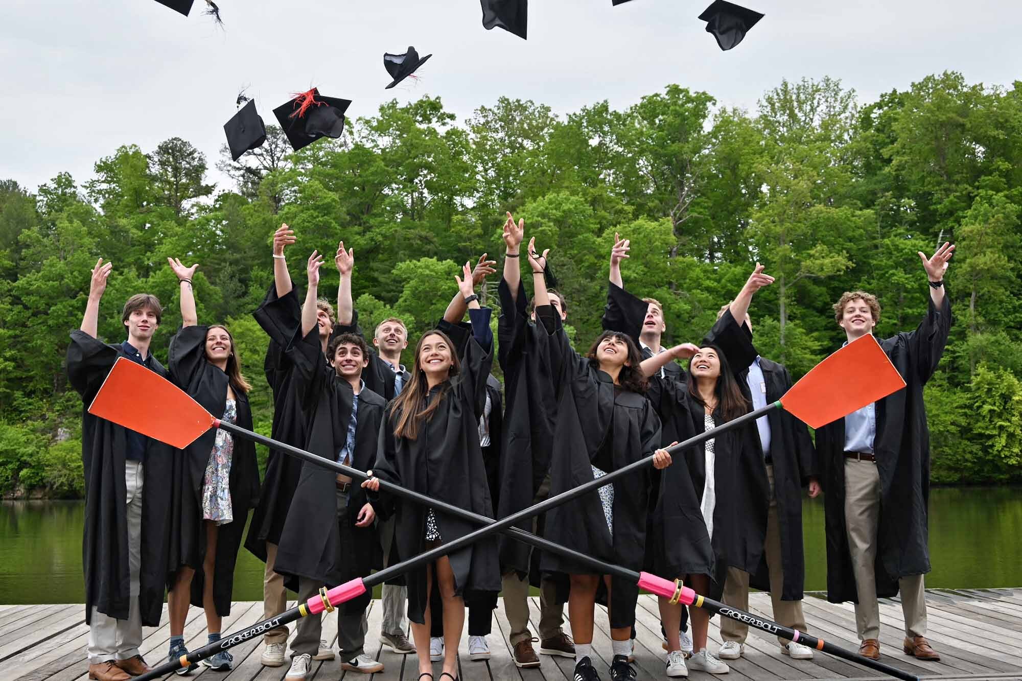 Group photo of the graduating members of the UVA rowing teams with two oars across them and throwing their hats in the air