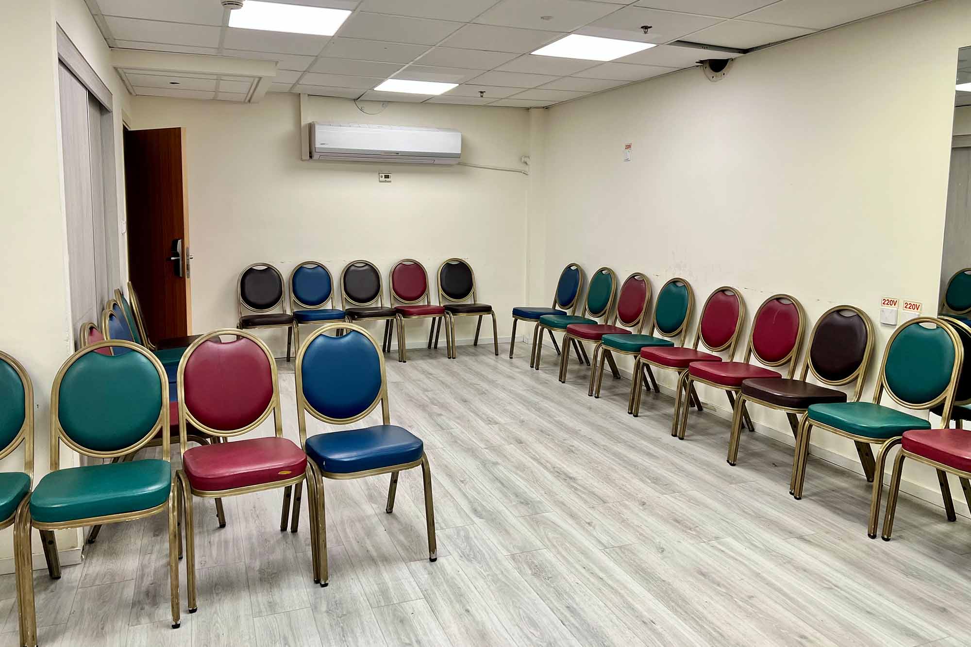 Empty room with colorful chairs arranged in a circle under bright ceiling lights.