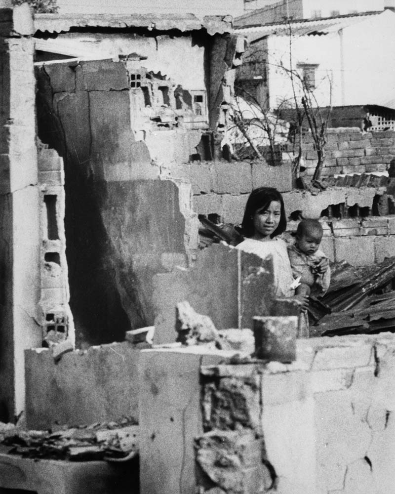 A portrait of a girl holding a baby inside a building ruined by war.