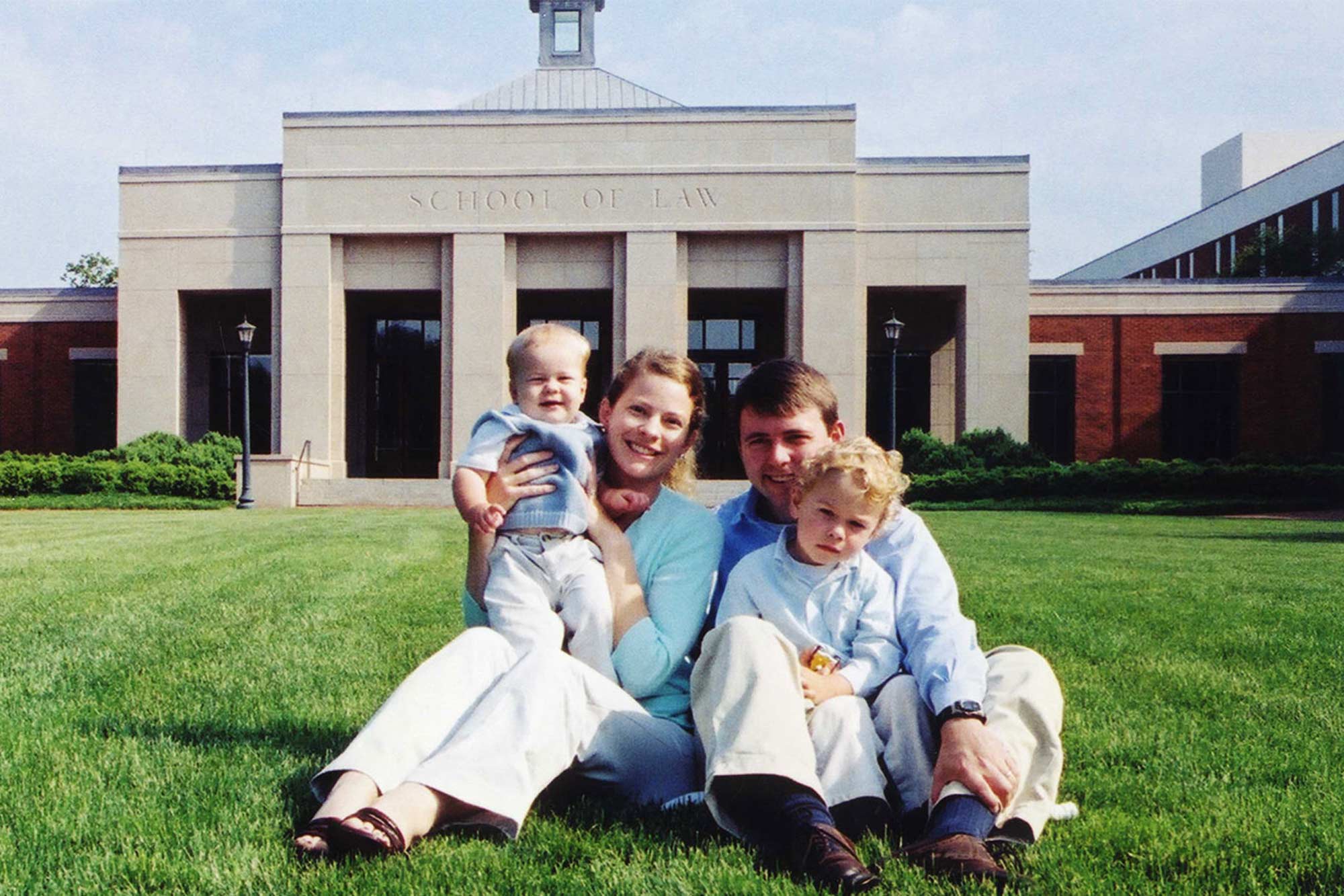 a family photo of Ryan and April Shores with their children sitting on the grass in front of the UVA Law School