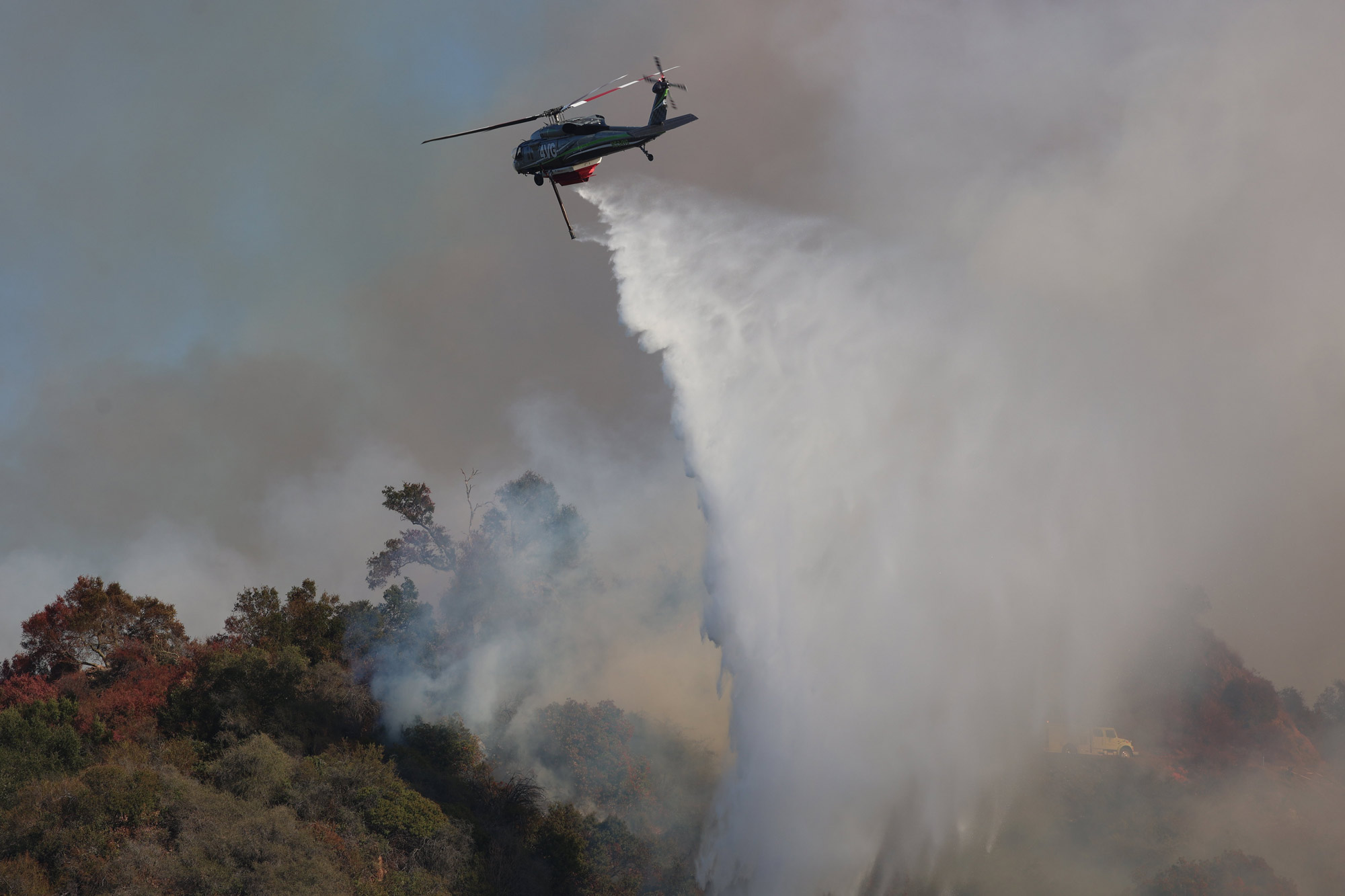 Airborne firefighters in a helicopter drop water on the Palisades fire.