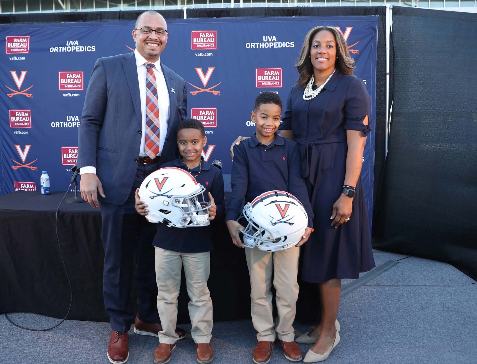 Tony Elliot, Ace Elliot, A.J. Elliot, and Tamika Elliot pose for a photo in front of a UVA football background. The two boys are holding UVA football helmets.