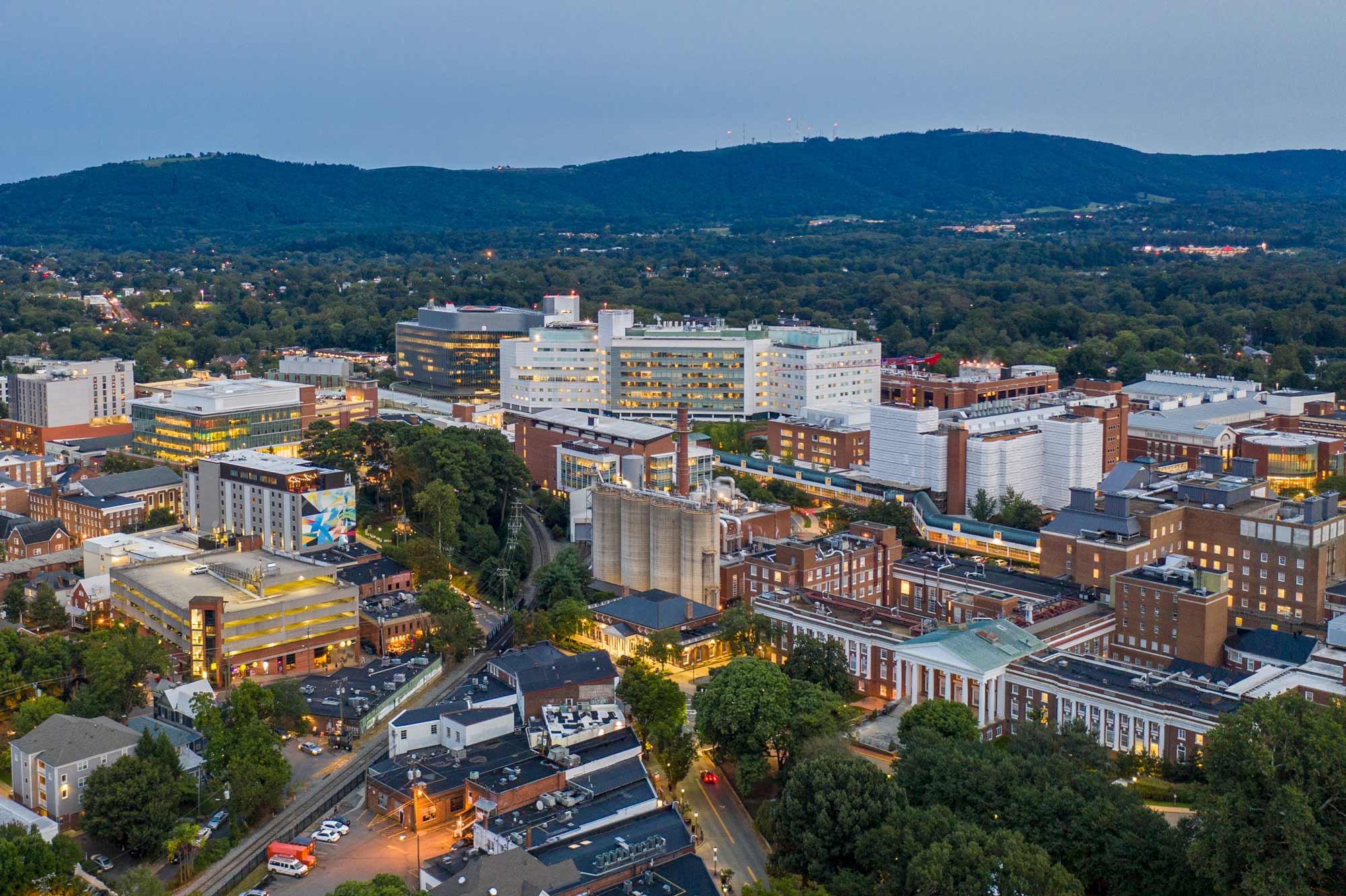 Aerial view of the UVA Health University Medical Center and surrounding buildings in Charlottesville, Virginia, with the Blue Ridge Mountains in the background.