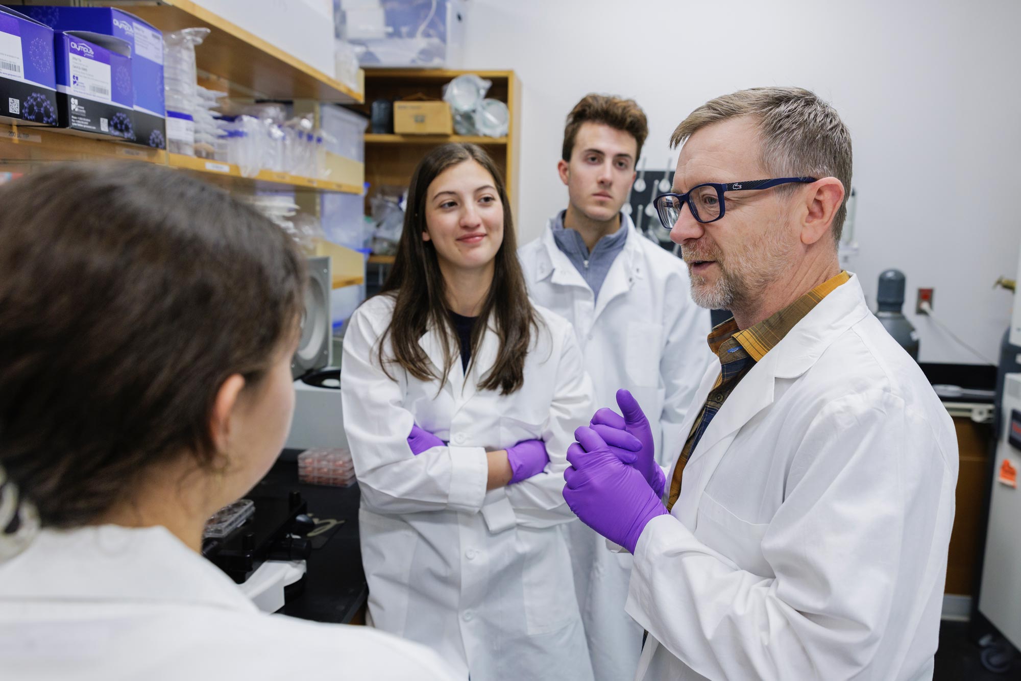 Grace Burns with two other students listening to Tom Baker in a lab