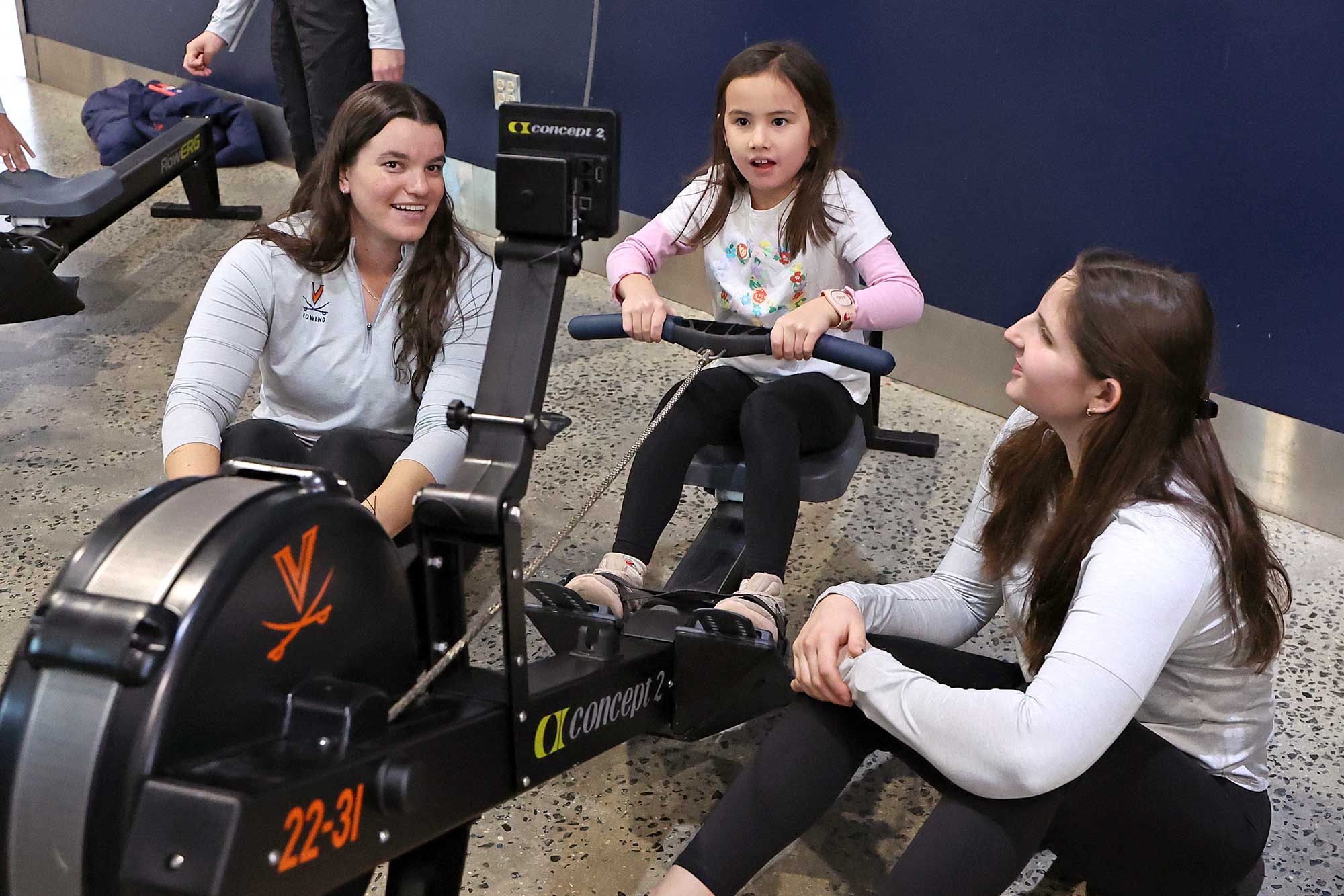 UVA graduate student Ryleigh Katstra, left, and freshman Peyton Balazy teach a young fan how to use a rowing machine.