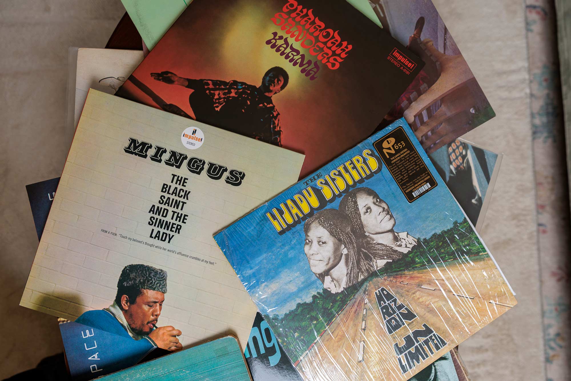a group of vinyl records in sleeves on a coffee table from ‘Mingus’, ‘Pharoah Sanders’, and ‘the Lijadu Sisters’. 